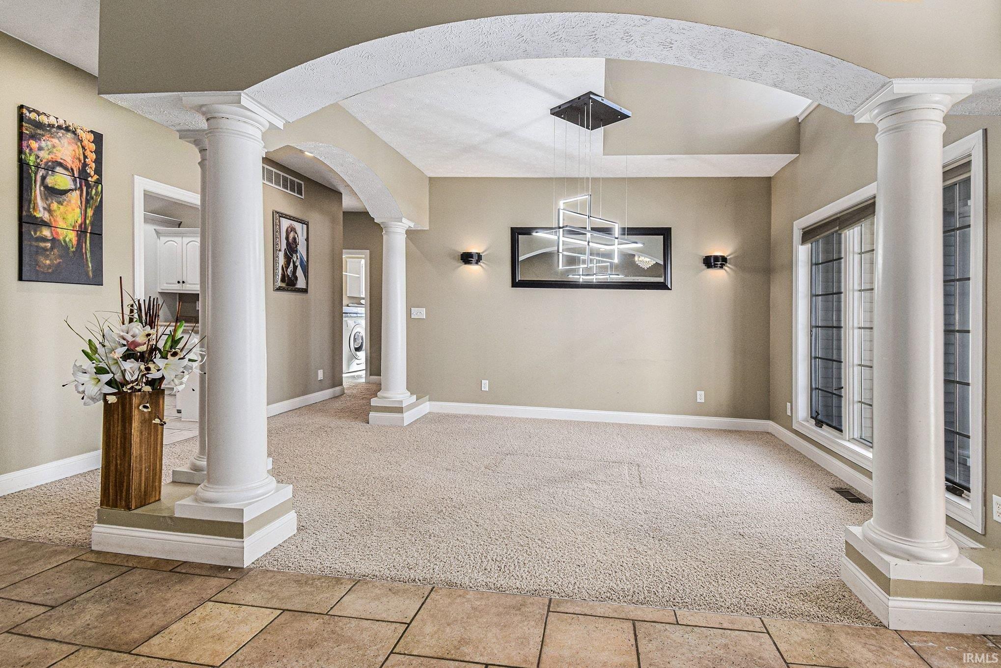 Foyer entrance with ornate columns, light colored carpet, washer / dryer, and arched walkways