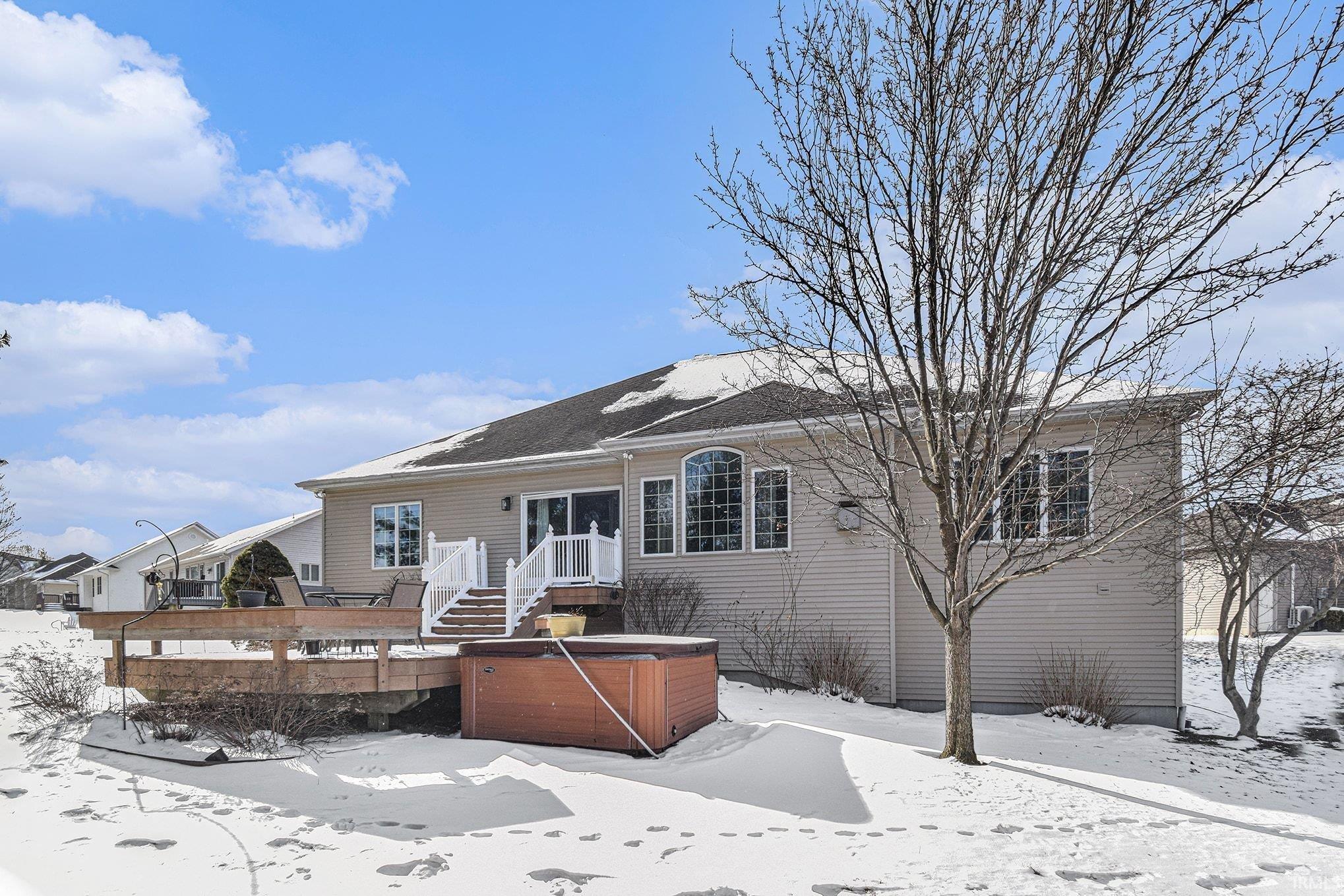 Snow covered house with a hot tub and a wooden deck