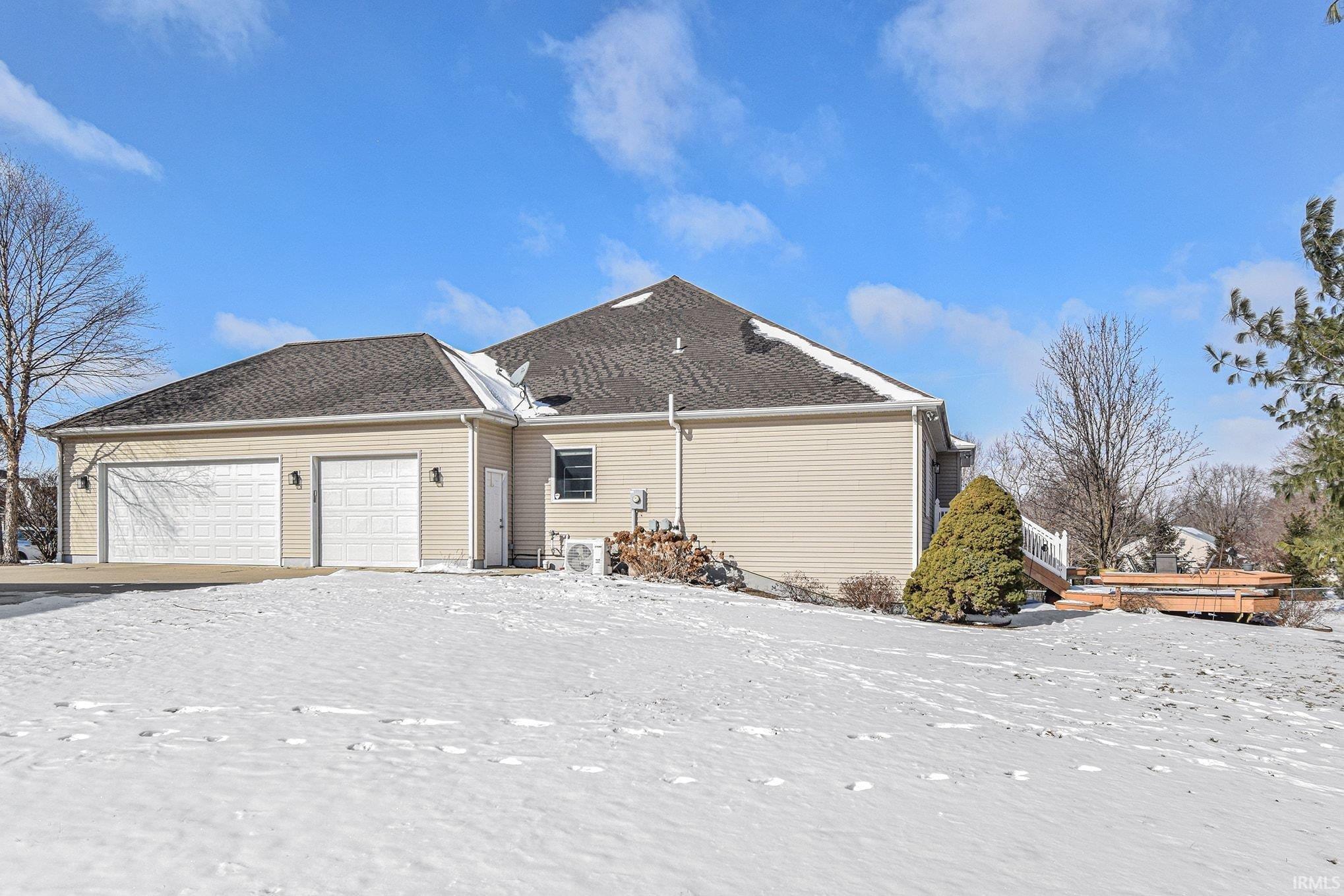 Snow covered back of property featuring an attached garage and roof with shingles
