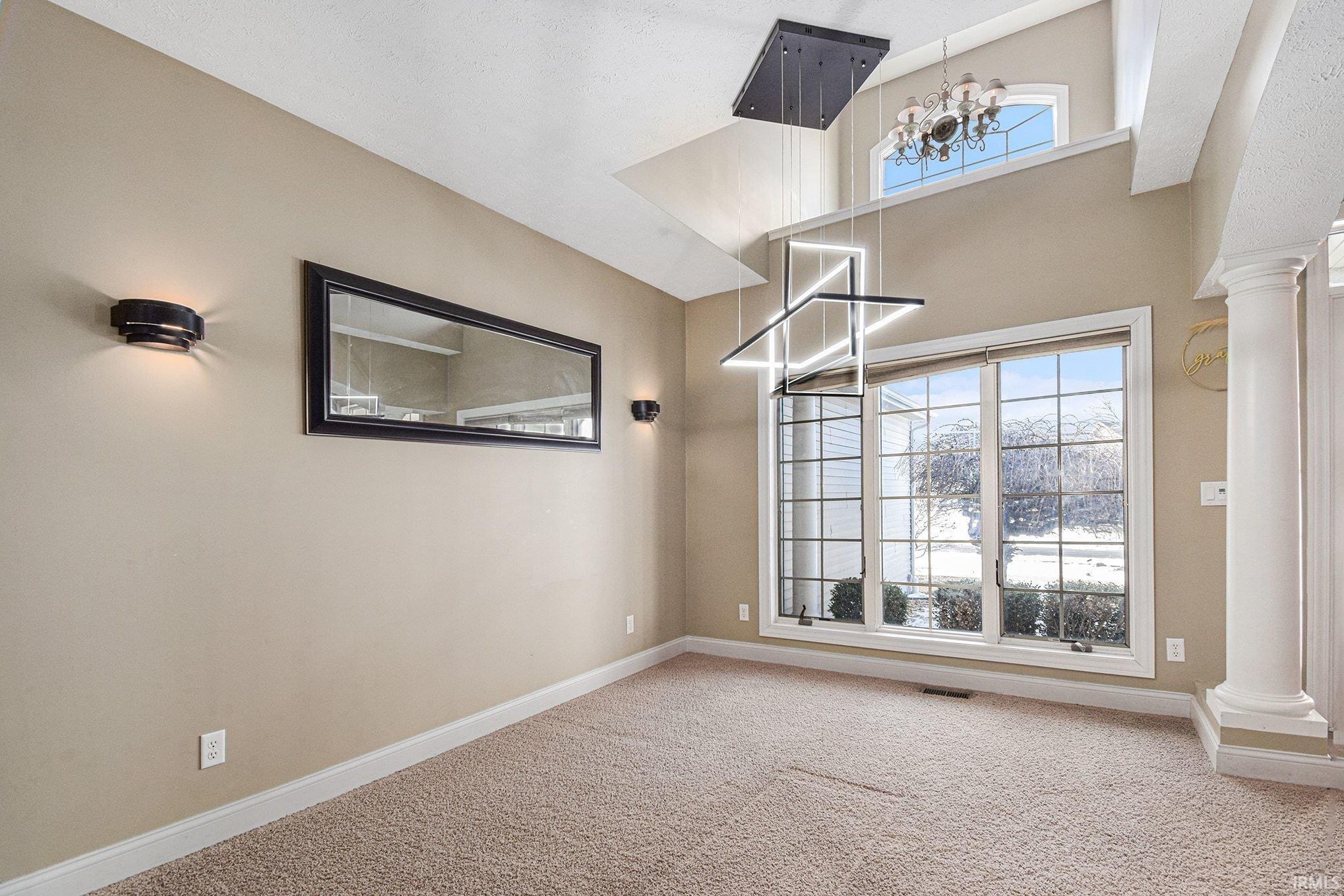 Carpeted spare room with ornate columns, a high ceiling, and a chandelier