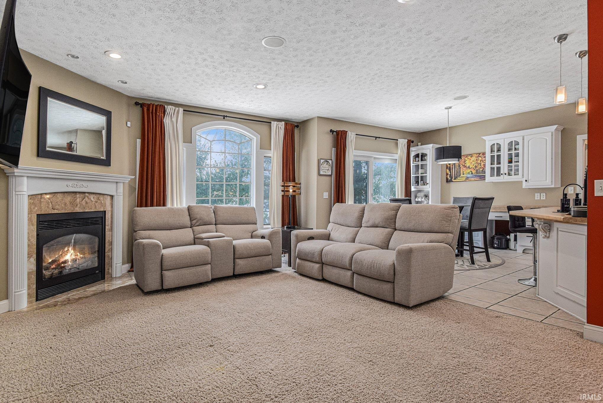 Living room with a high end fireplace, healthy amount of natural light, a textured ceiling, light carpet, and light tile patterned floors