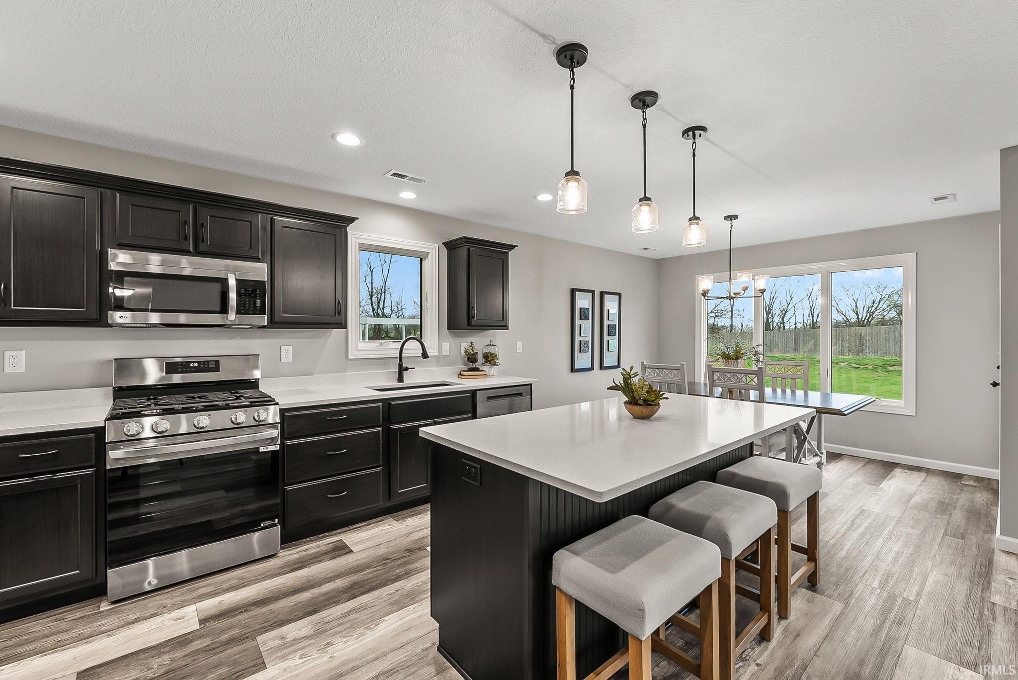 Kitchen with stainless steel appliances, a kitchen island, a kitchen bar, light wood-style floors, and dark cabinets