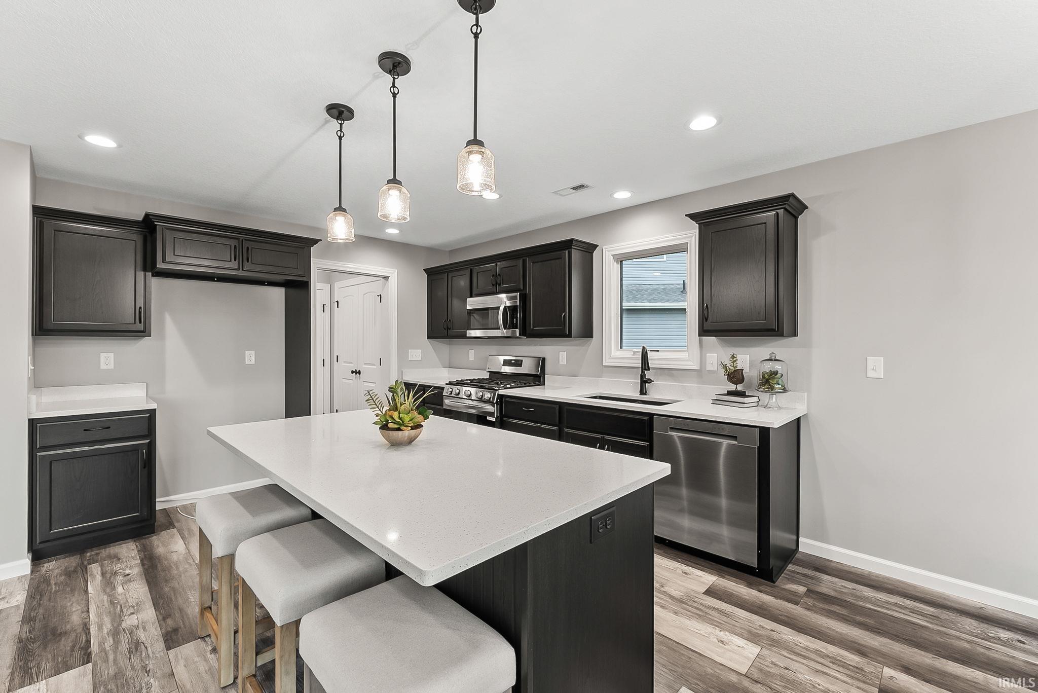 Kitchen with a breakfast bar area, stainless steel appliances, light wood-style floors, a center island, and decorative light fixtures