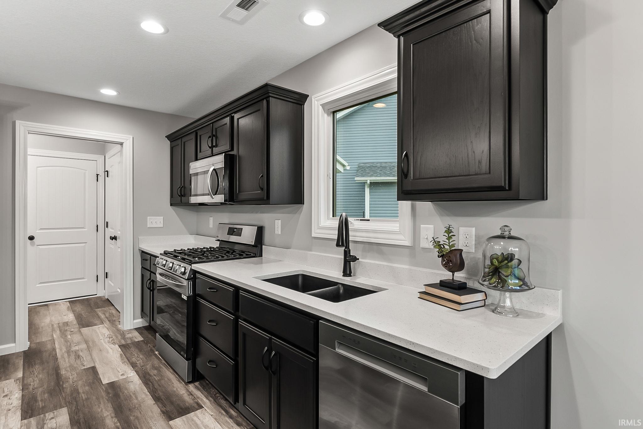Kitchen featuring dark cabinetry, stainless steel appliances, light stone countertops, dark wood-style flooring, and recessed lighting