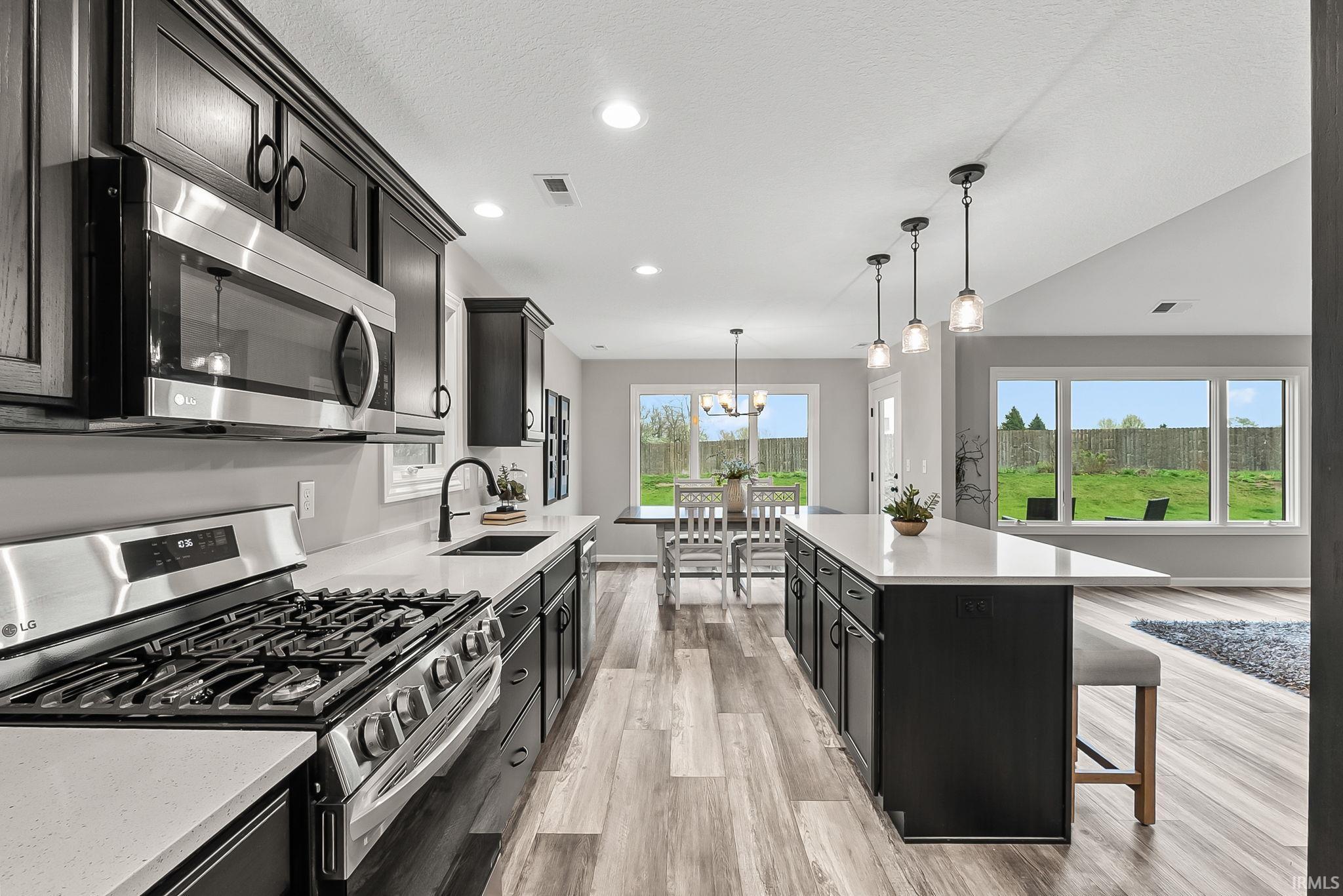 Kitchen with stainless steel appliances, dark cabinets, light wood-style floors, light stone countertops, and a center island