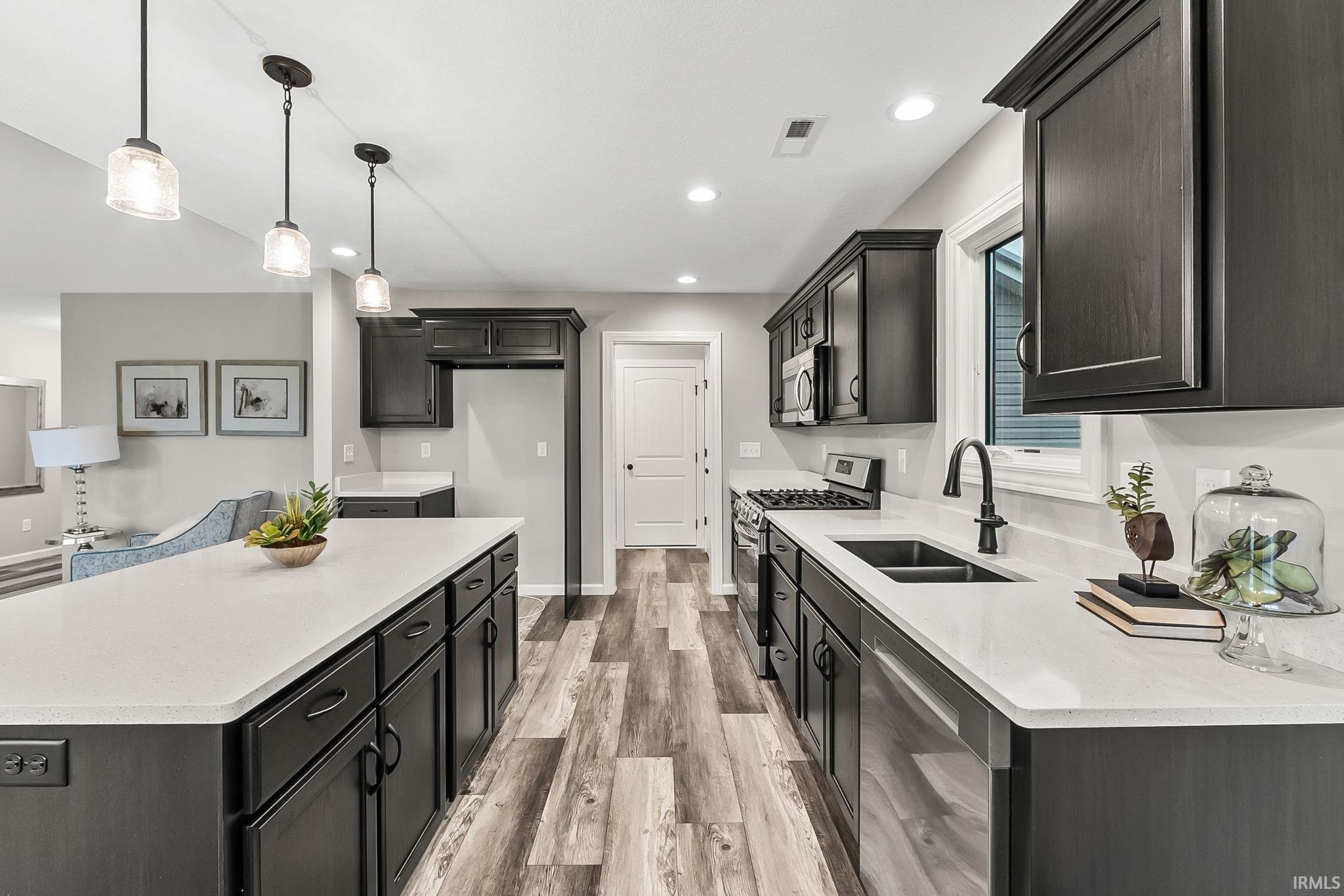 Kitchen with stainless steel appliances, light wood finished floors, light stone counters, hanging light fixtures, and a center island