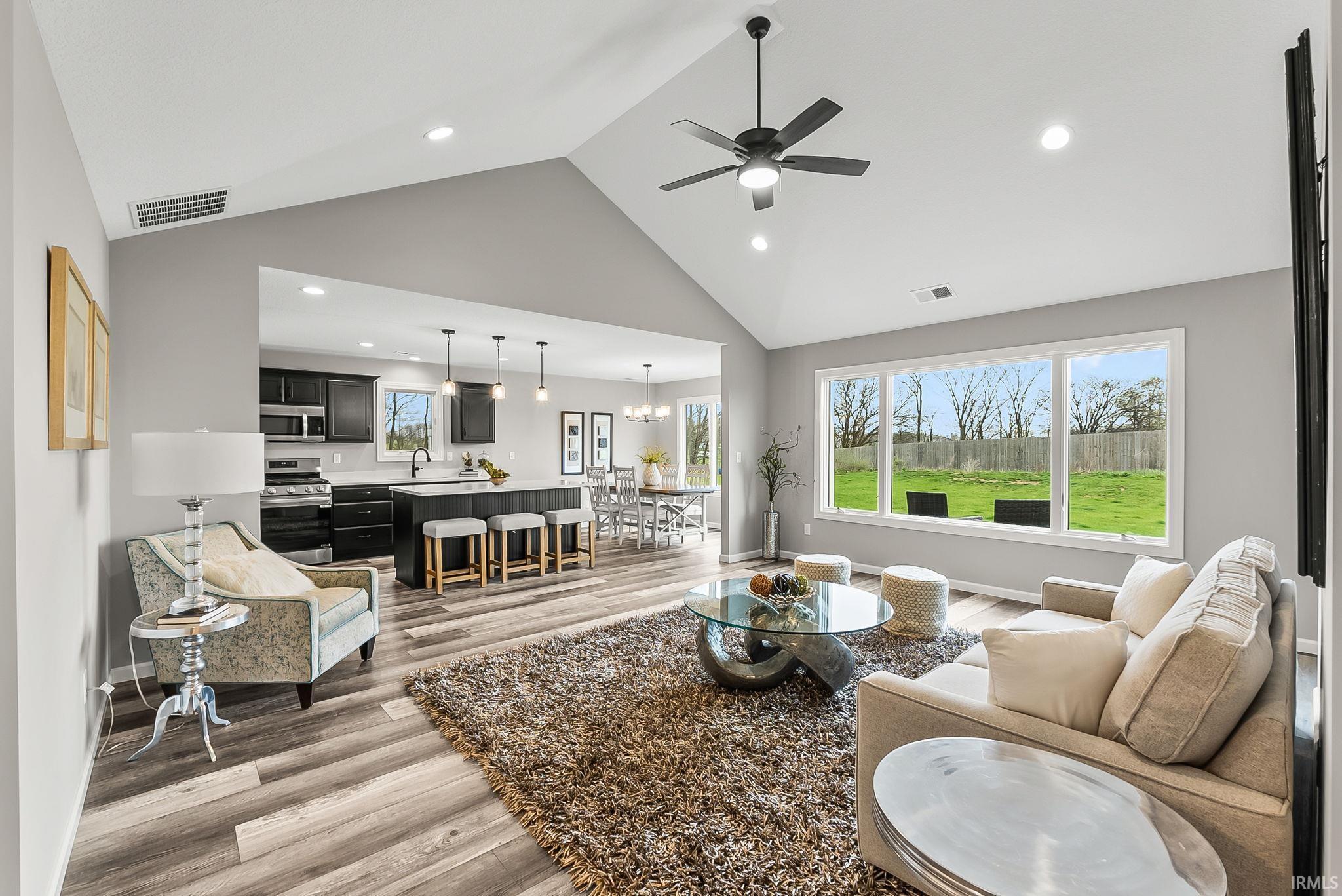 Living room with ceiling fan, light wood finished floors, a high ceiling, and suspended lighting