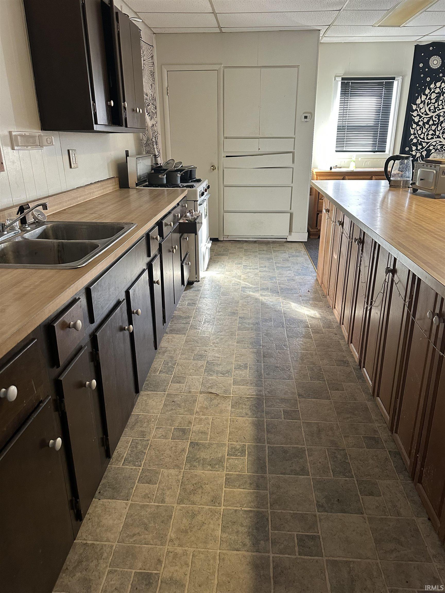 Kitchen featuring a drop ceiling, gas stove, light countertops, and brick patterned flooring