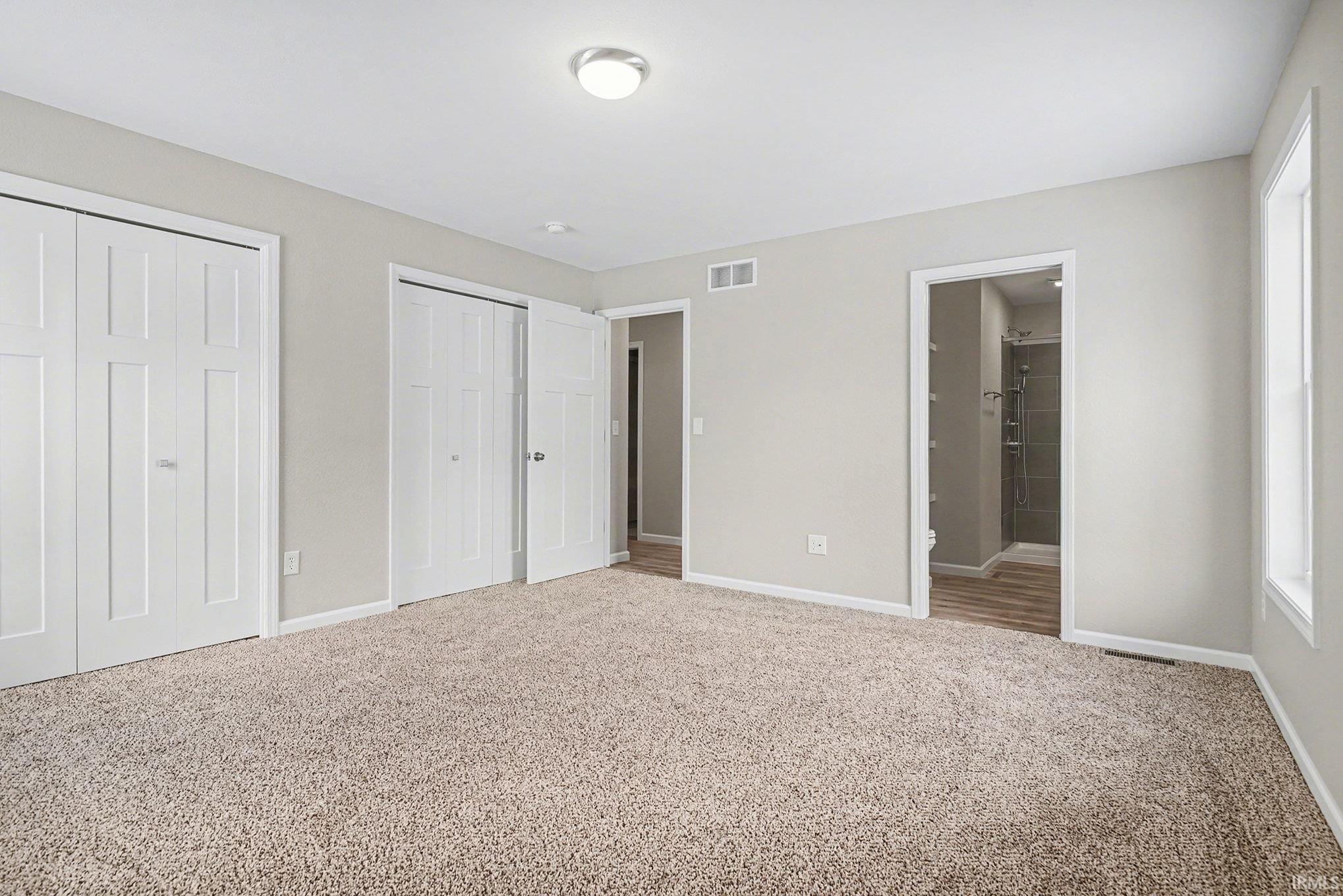 Unfurnished bedroom featuring multiple closets, carpet, and ensuite bathroom