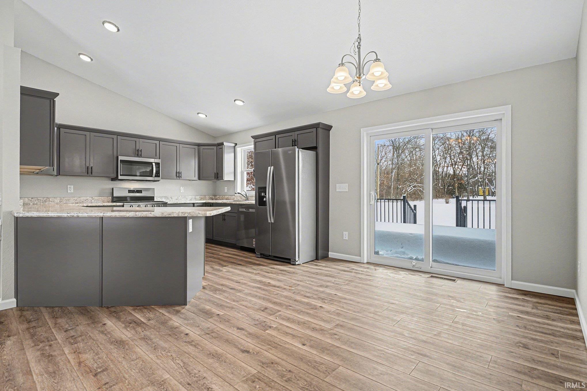 Kitchen featuring a peninsula, stainless steel appliances, pendant lighting, light stone countertops, and light wood-style floors