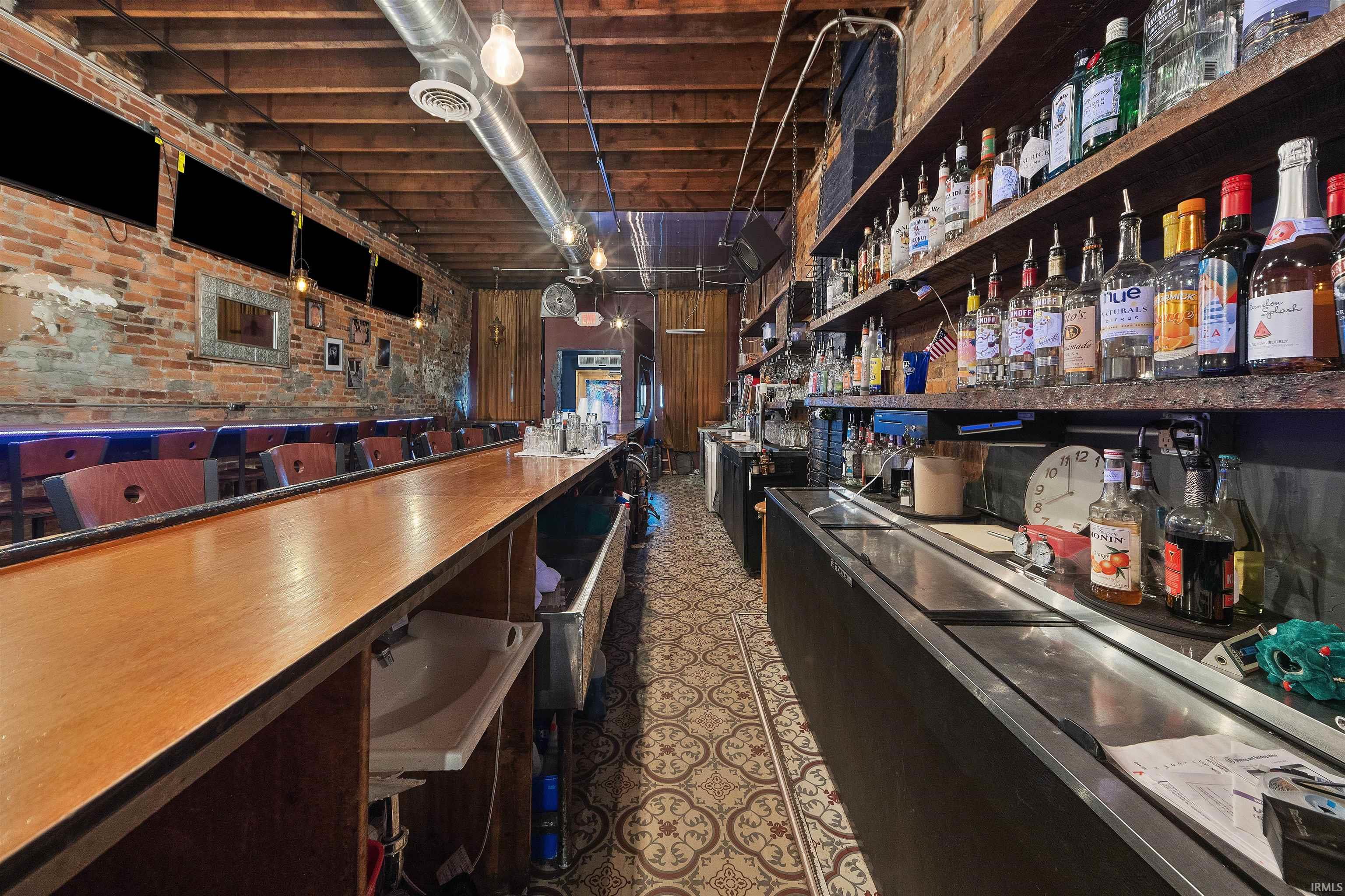 Community bar area featuring brick wall, open shelves, butcher block countertops, and dark cabinetry