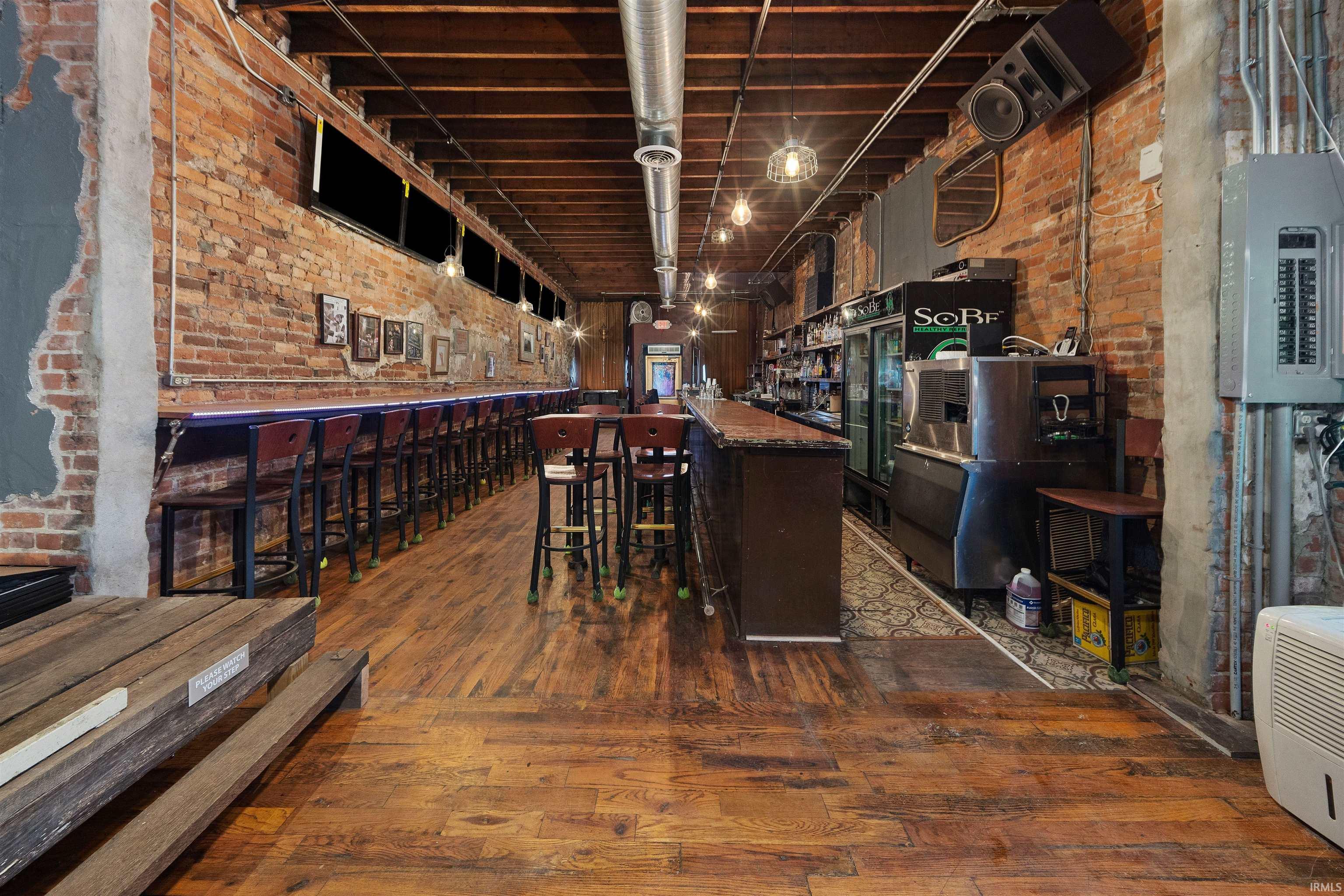 Community bar area with brick wall, electric panel, dark stone countertops, and dark brown cabinetry
