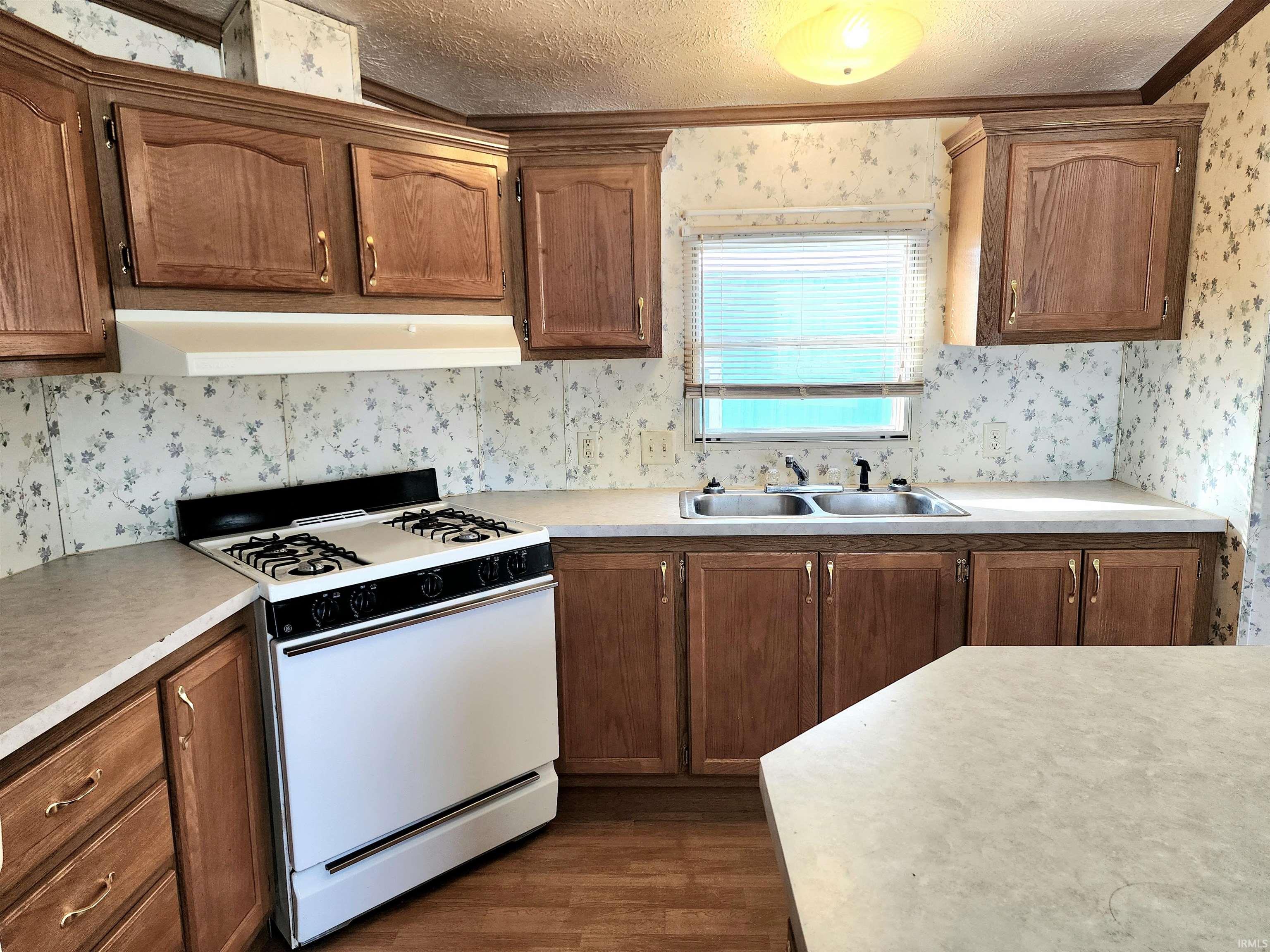 Kitchen with wallpapered walls, white range with gas stovetop, a textured ceiling, light countertops, and under cabinet range hood