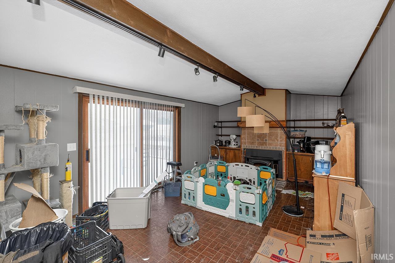 Living room featuring wood walls, beam ceiling, and brick patterned floors