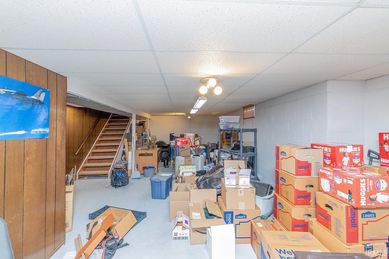Finished basement with a paneled ceiling, concrete block wall, and stairs