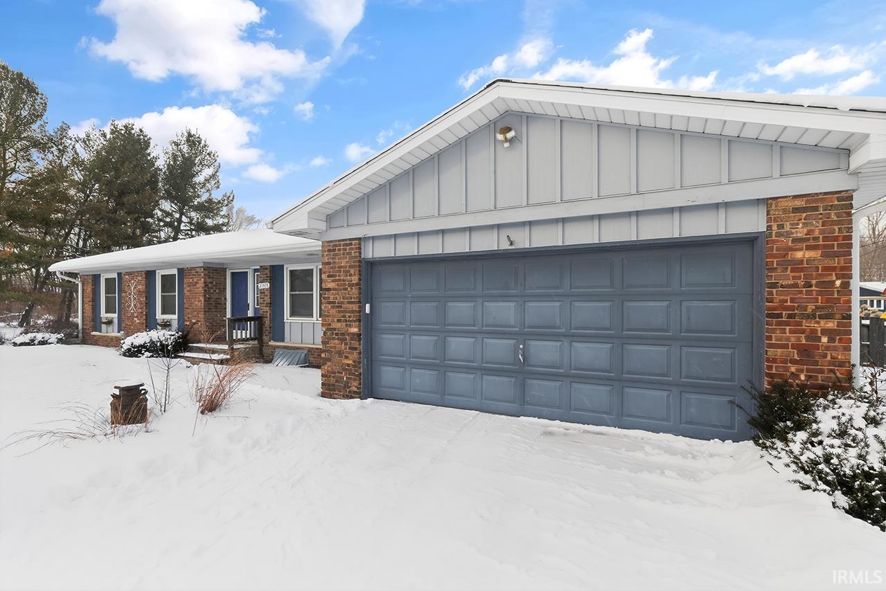 Ranch-style house with board and batten siding, brick siding, an attached garage, and a porch