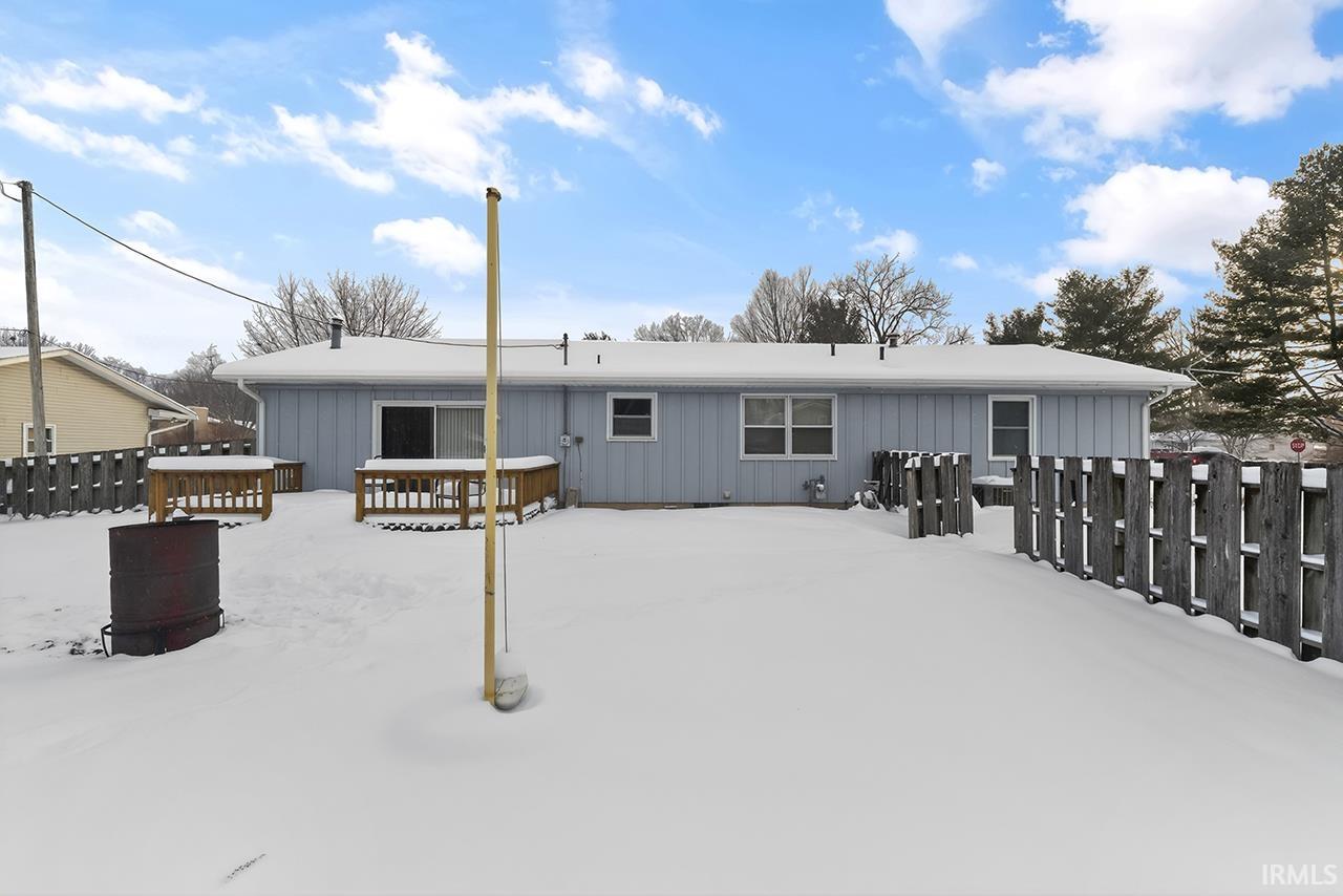Snow covered back of property featuring board and batten siding and a wooden deck