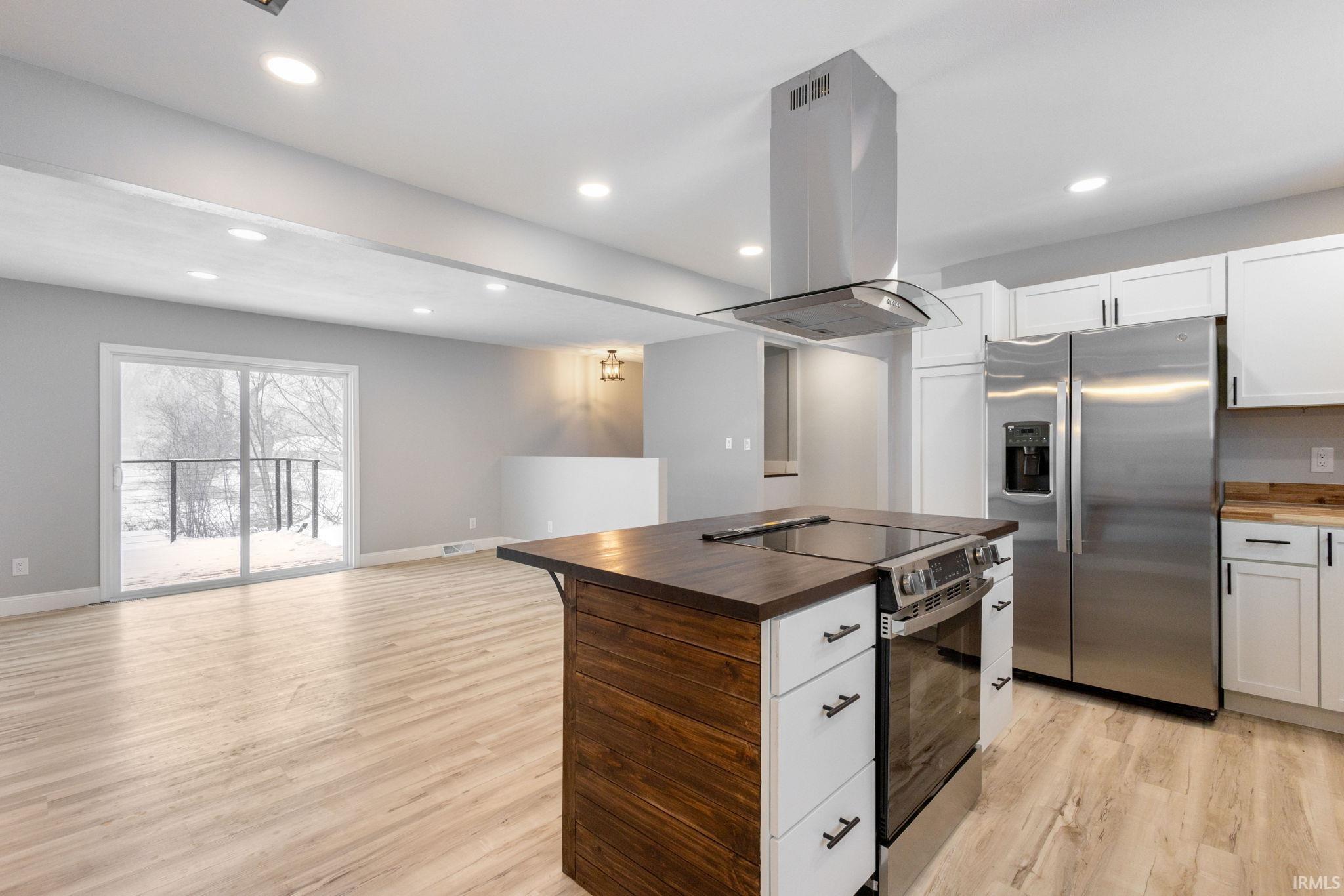 Kitchen featuring butcher block counters, range with electric cooktop, stainless steel refrigerator with ice dispenser, island range hood, and open floor plan