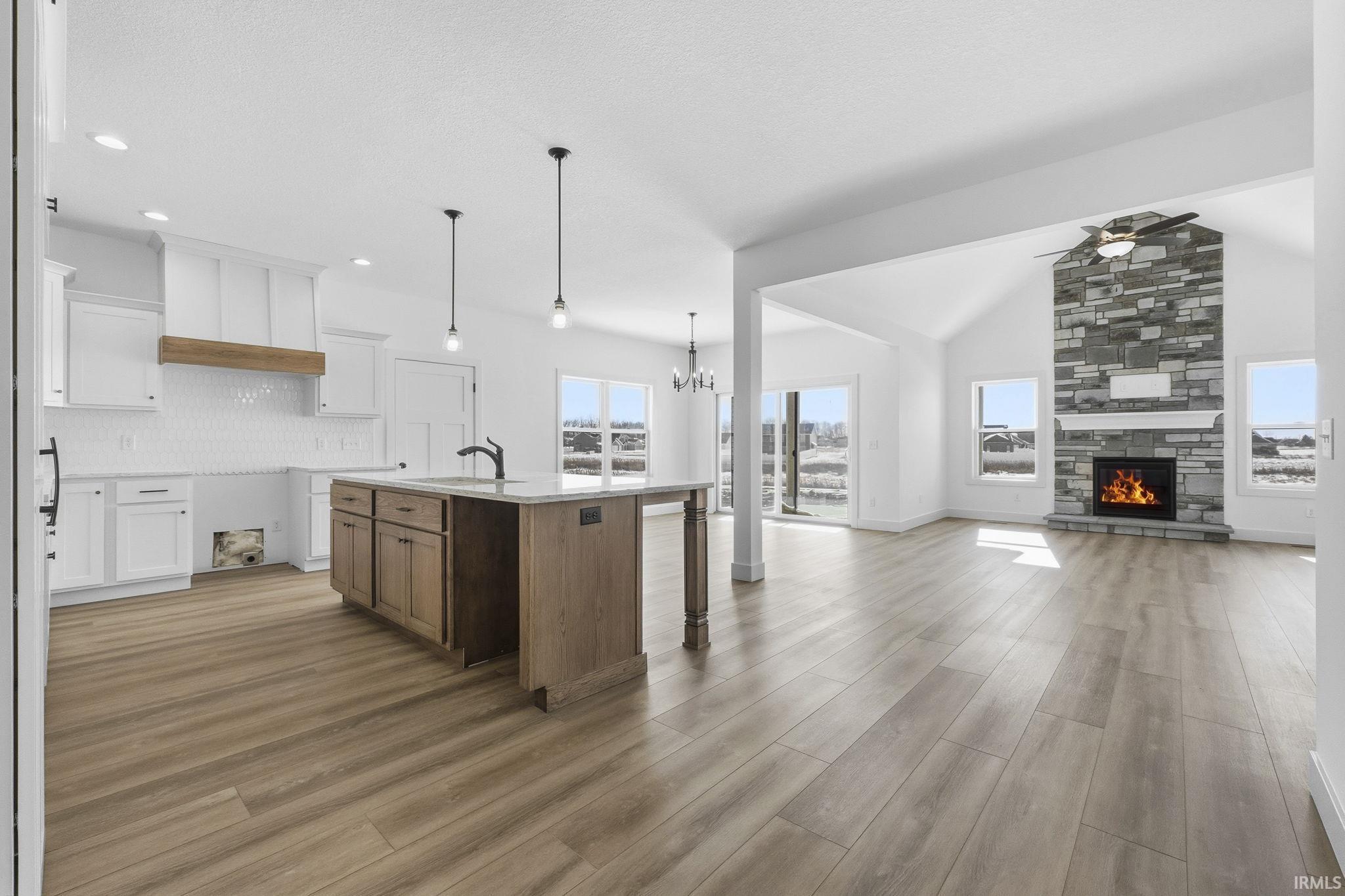 Kitchen featuring white cabinetry, a kitchen bar, a center island with sink, a fireplace, and light wood-type flooring
