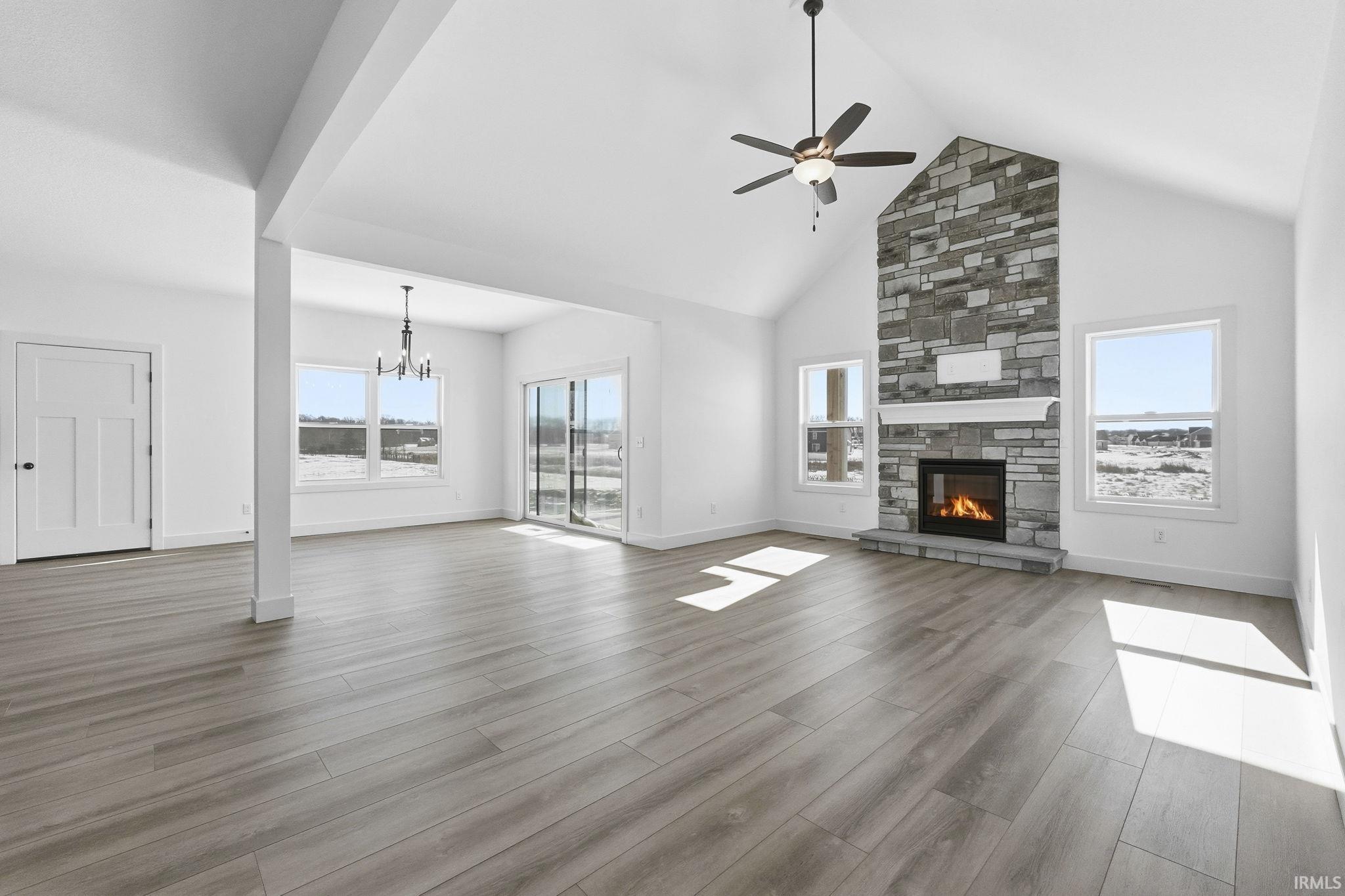 Unfurnished living room featuring high vaulted ceiling, a fireplace, a ceiling fan, a chandelier, and wood finished floors