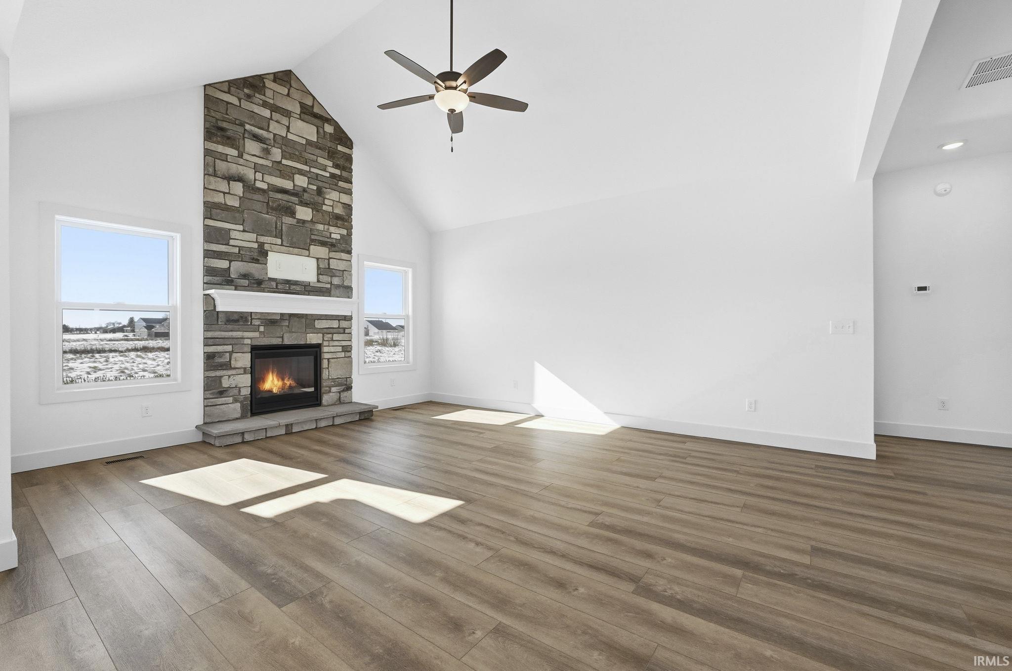 Unfurnished living room with high vaulted ceiling, wood finished floors, a fireplace, and a ceiling fan