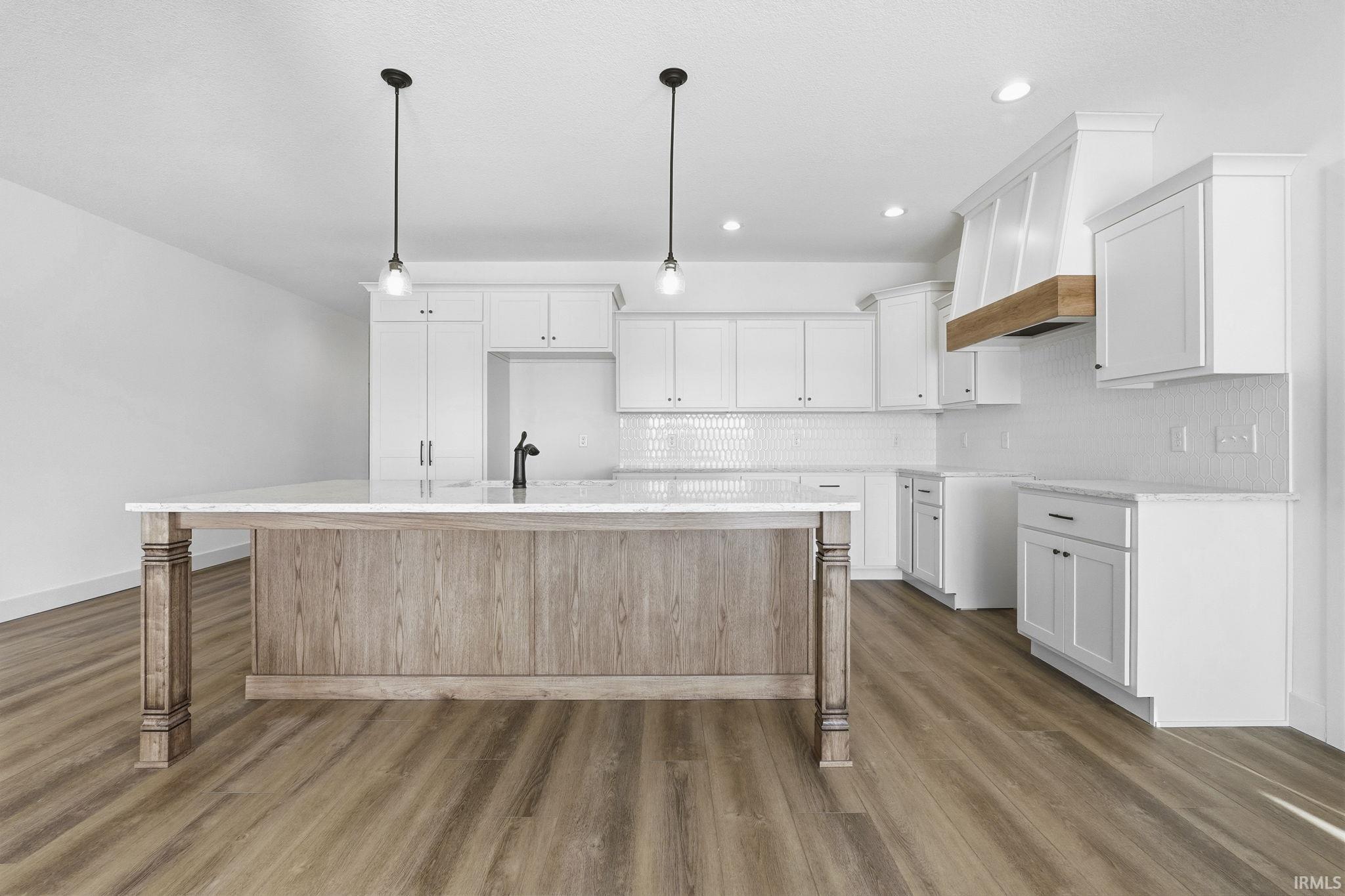 Kitchen featuring white cabinets, premium range hood, pendant lighting, a center island with sink, and decorative backsplash