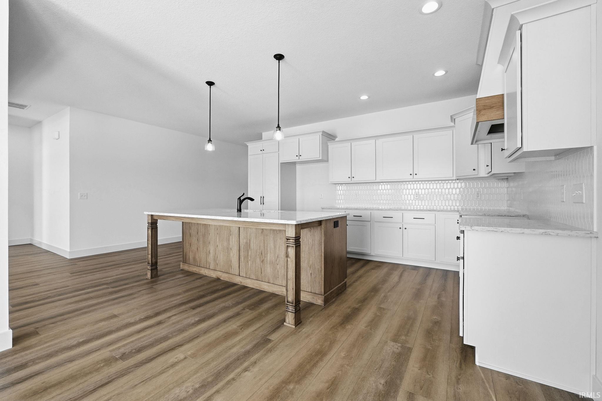 Kitchen featuring white cabinets, hanging light fixtures, backsplash, dark wood-style floors, and a kitchen island with sink