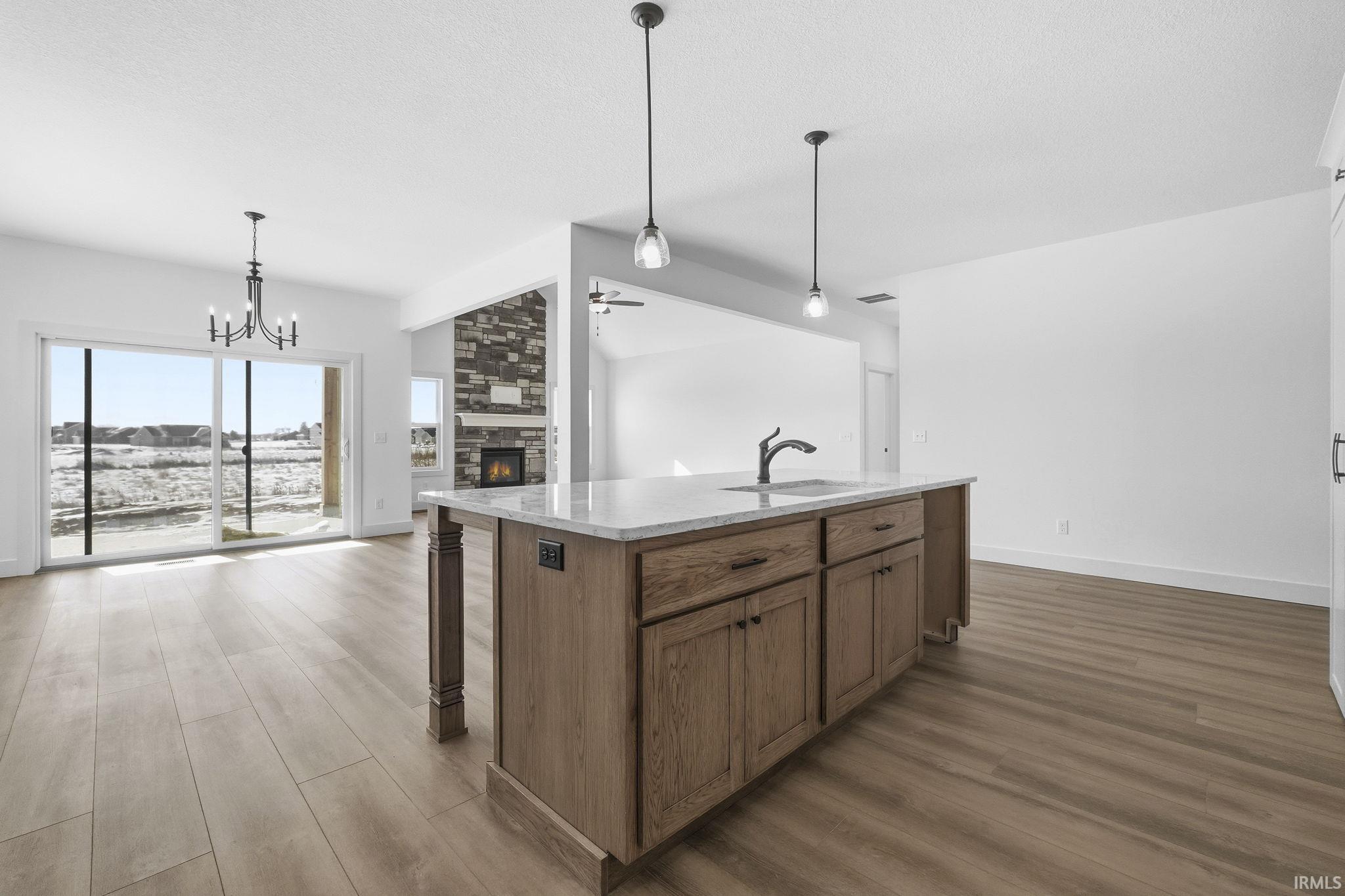 Kitchen featuring brown cabinetry, dark wood-style floors, light stone countertops, pendant lighting, and a chandelier