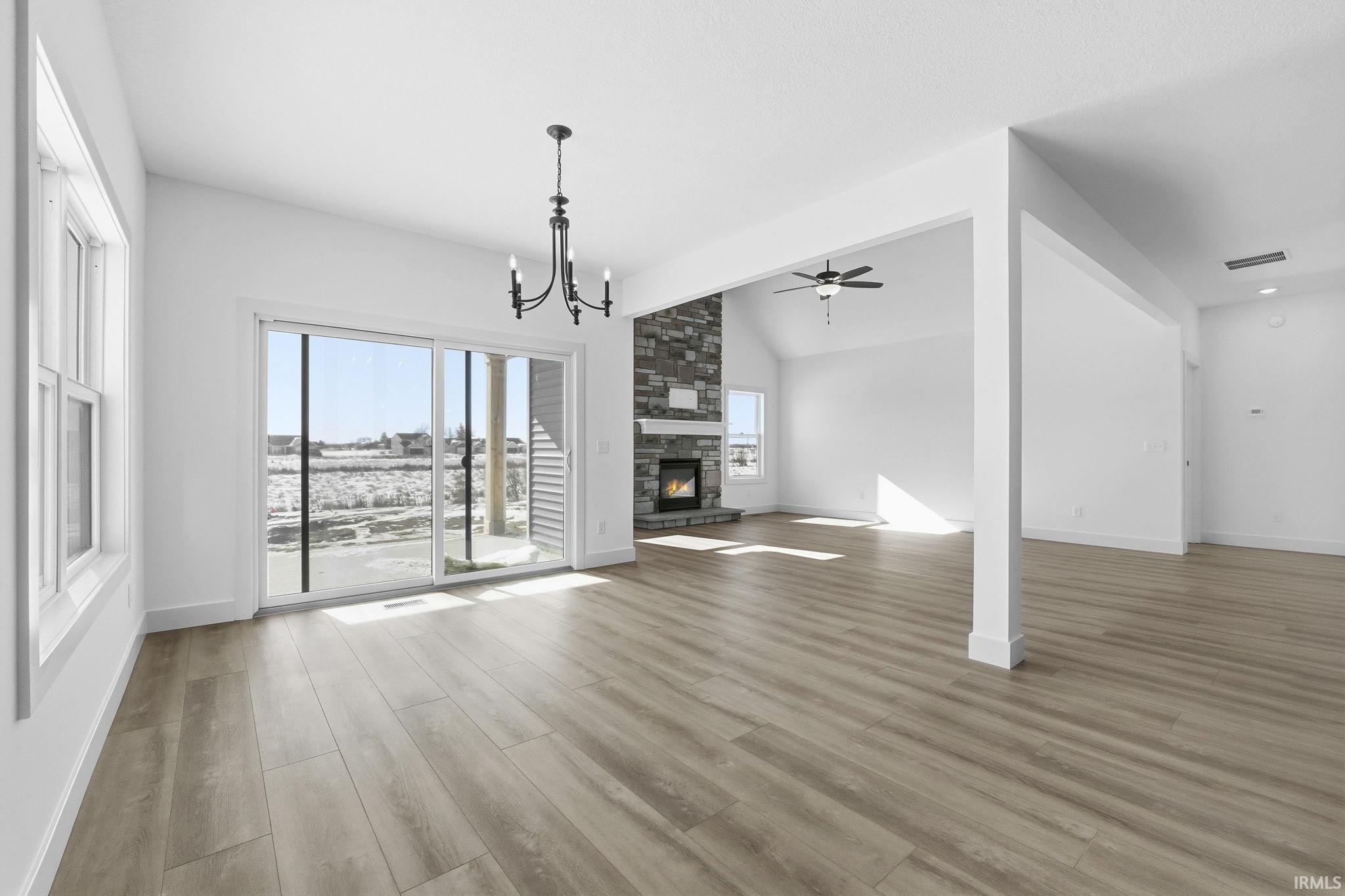 Unfurnished living room with a fireplace, light wood-style flooring, a chandelier, a ceiling fan, and lofted ceiling