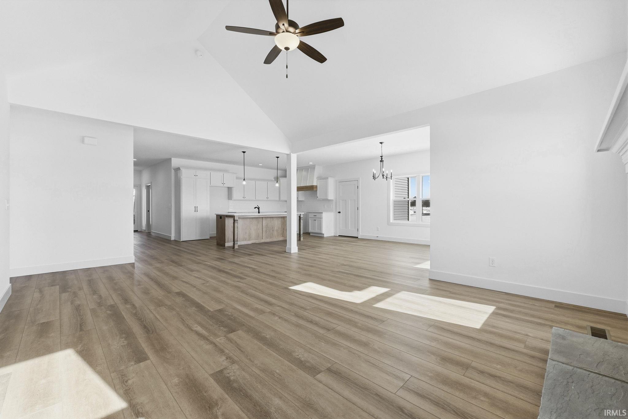 Unfurnished living room featuring high vaulted ceiling, light wood finished floors, ceiling fan, and a chandelier