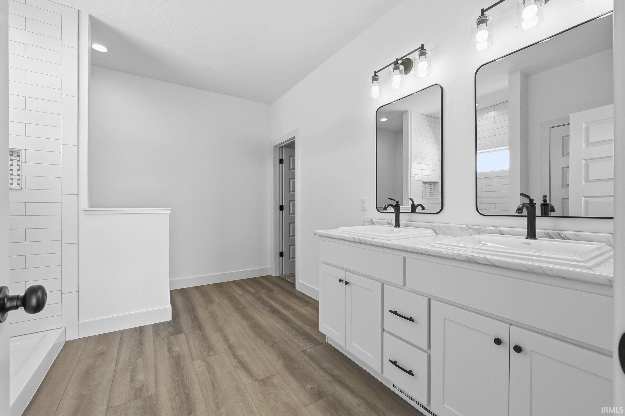 Bathroom featuring double vanity, light wood finished floors, recessed lighting, and a shower