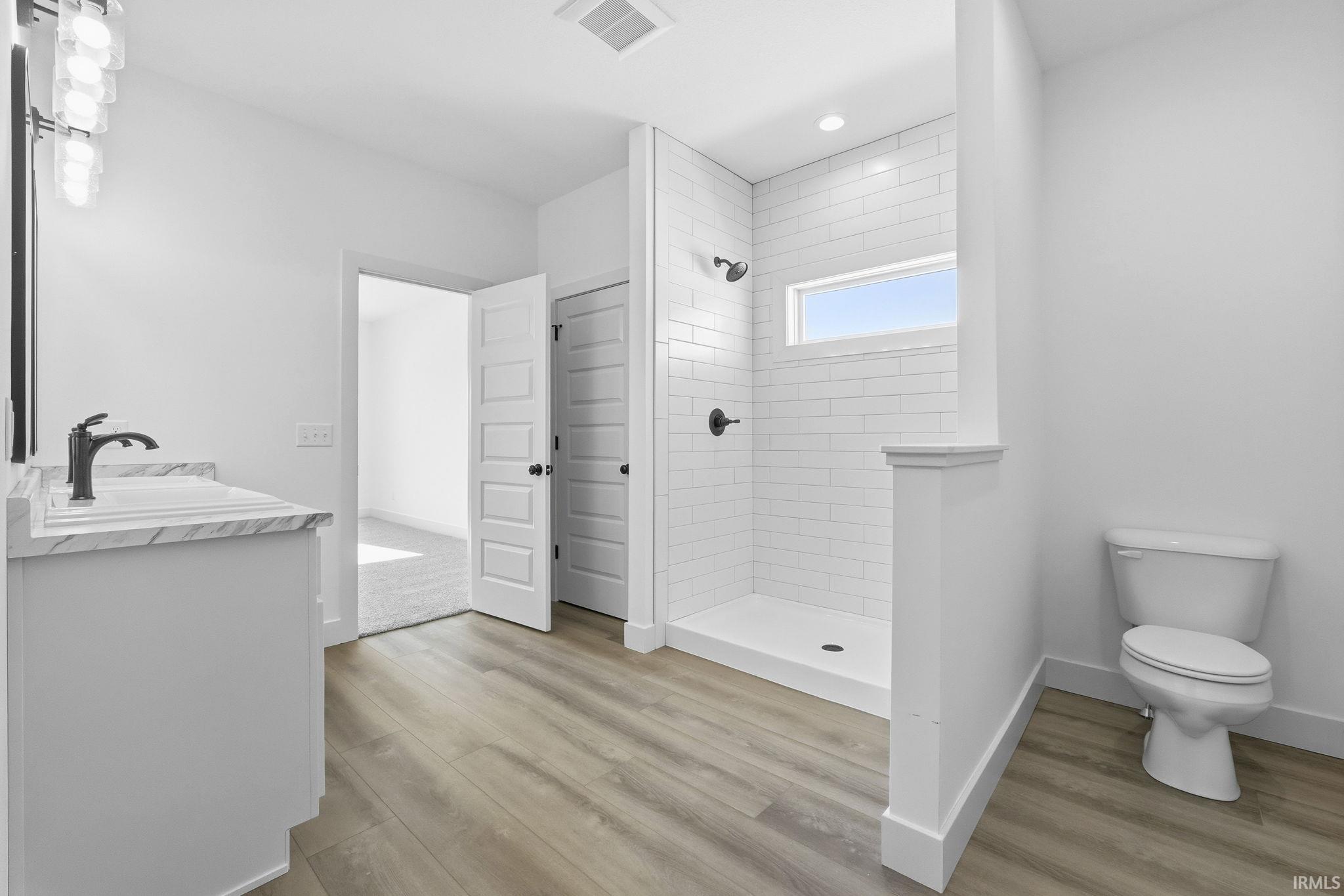 Full bathroom with tiled shower, vanity, and light wood-type flooring