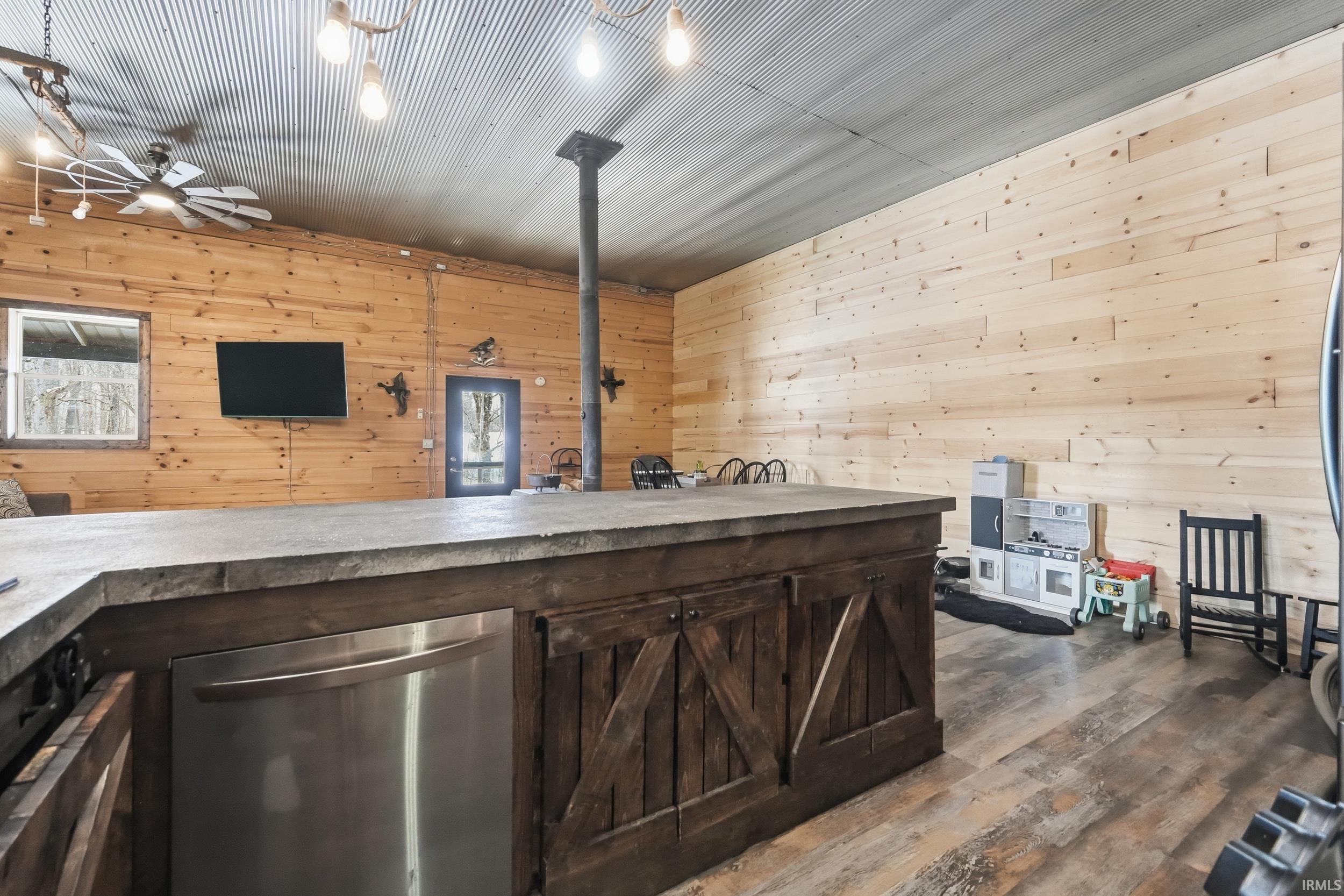 Bar area featuring wooden walls, dark brown cabinets, dishwasher, dark wood-style flooring, and light countertops