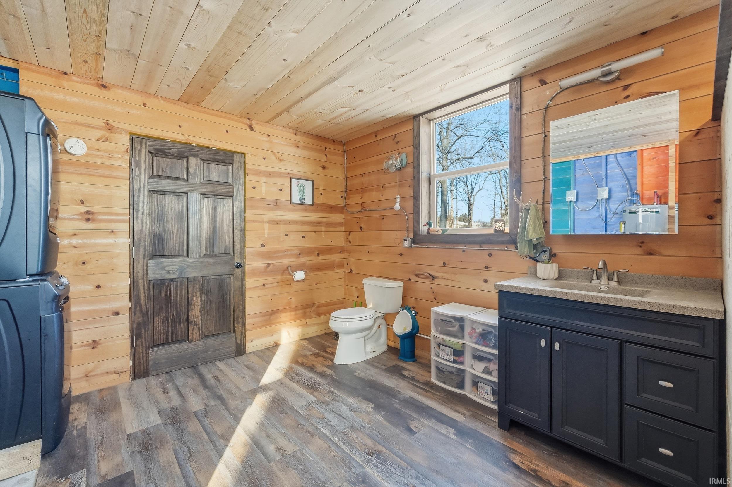Bathroom featuring vanity, wooden ceiling, wood walls, dark wood-type flooring, and stacked washing machine and dryer