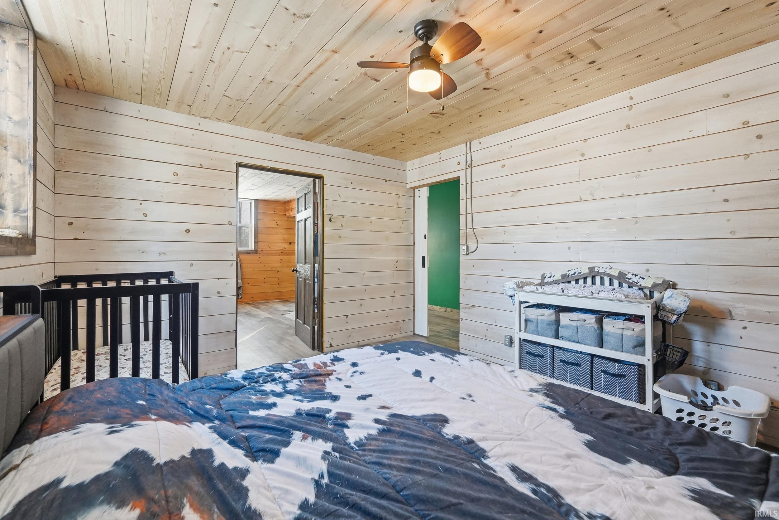 Bedroom featuring wooden walls, wooden ceiling, a crib, and a ceiling fan