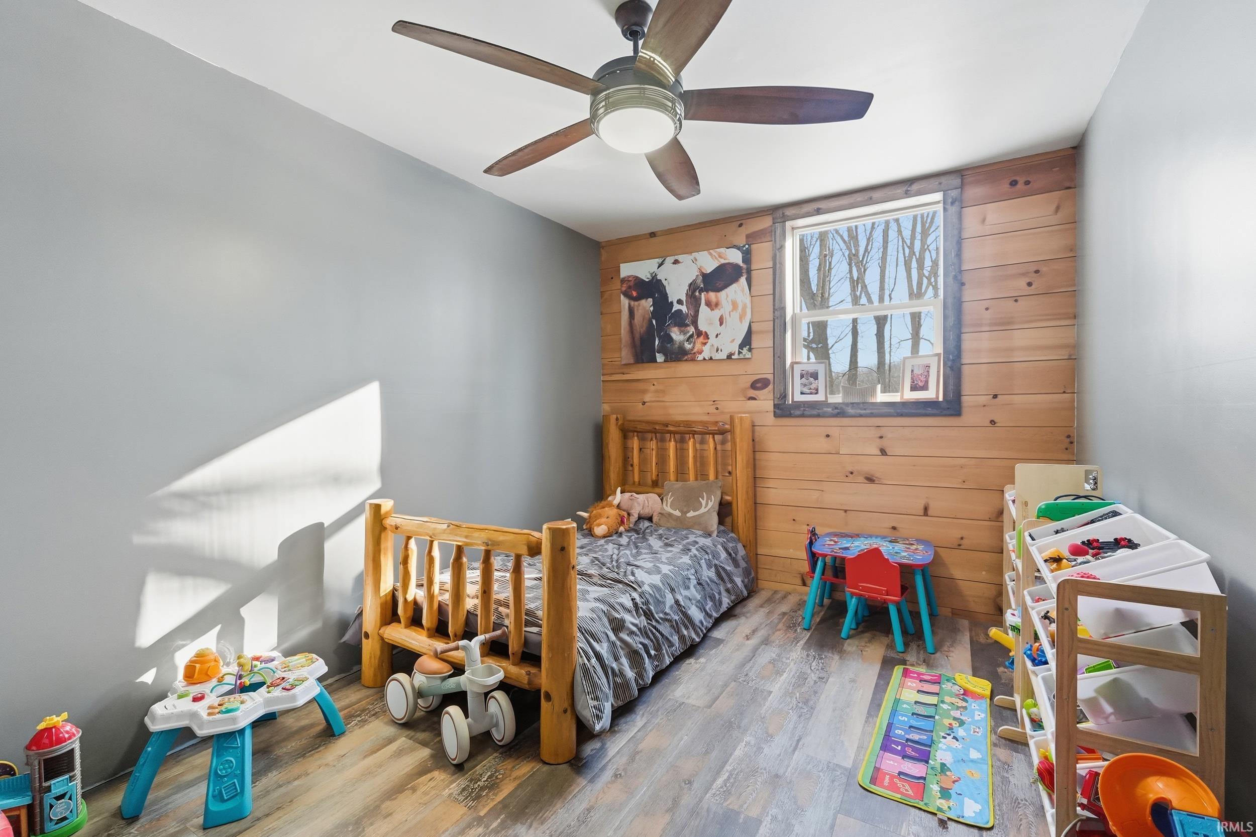 Bedroom with wood walls, wood finished floors, a ceiling fan, and an accent wall