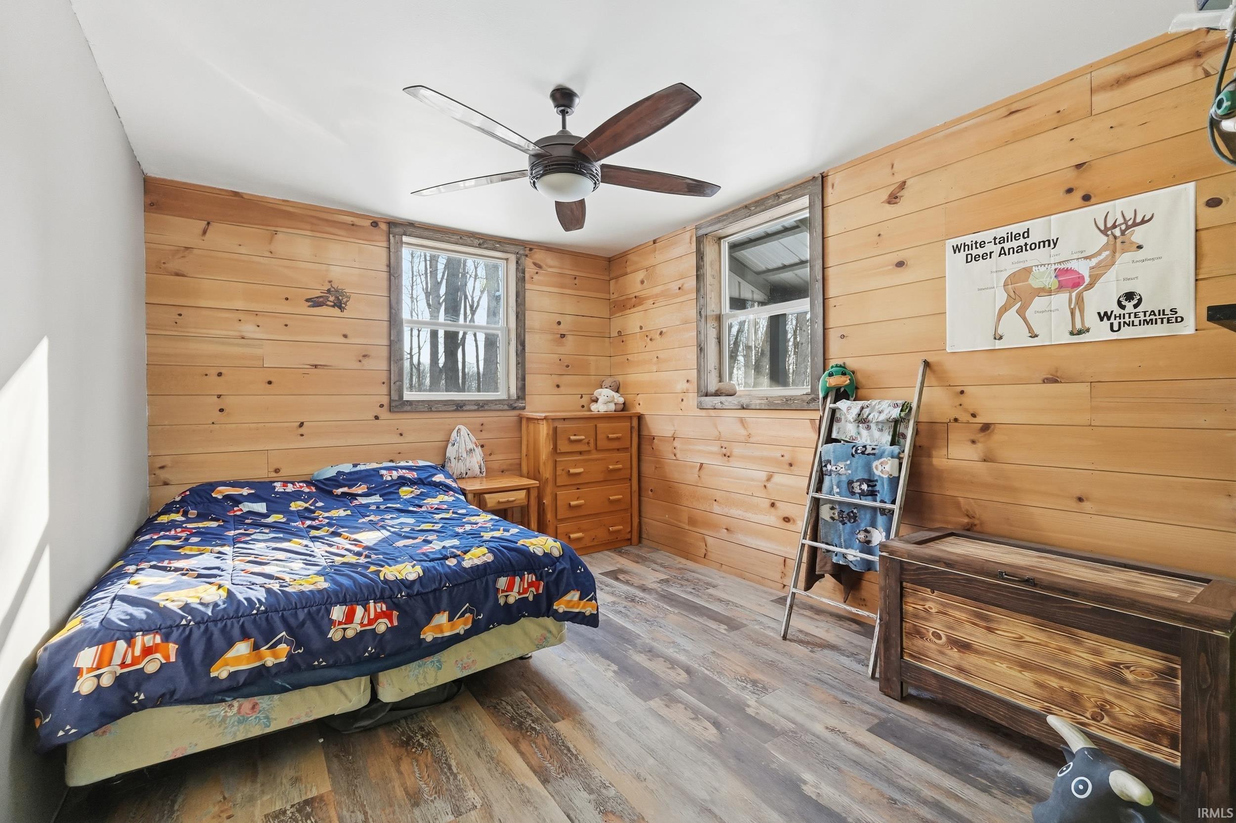 Bedroom featuring wooden walls, wood finished floors, and ceiling fan
