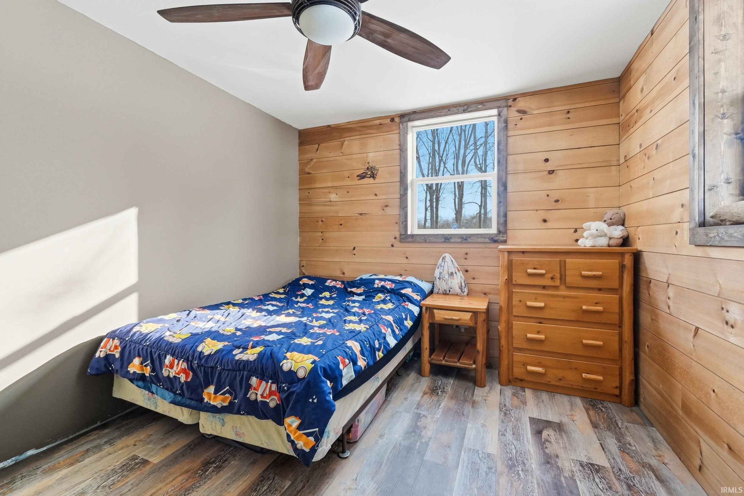 Bedroom featuring wood walls, wood finished floors, and a ceiling fan