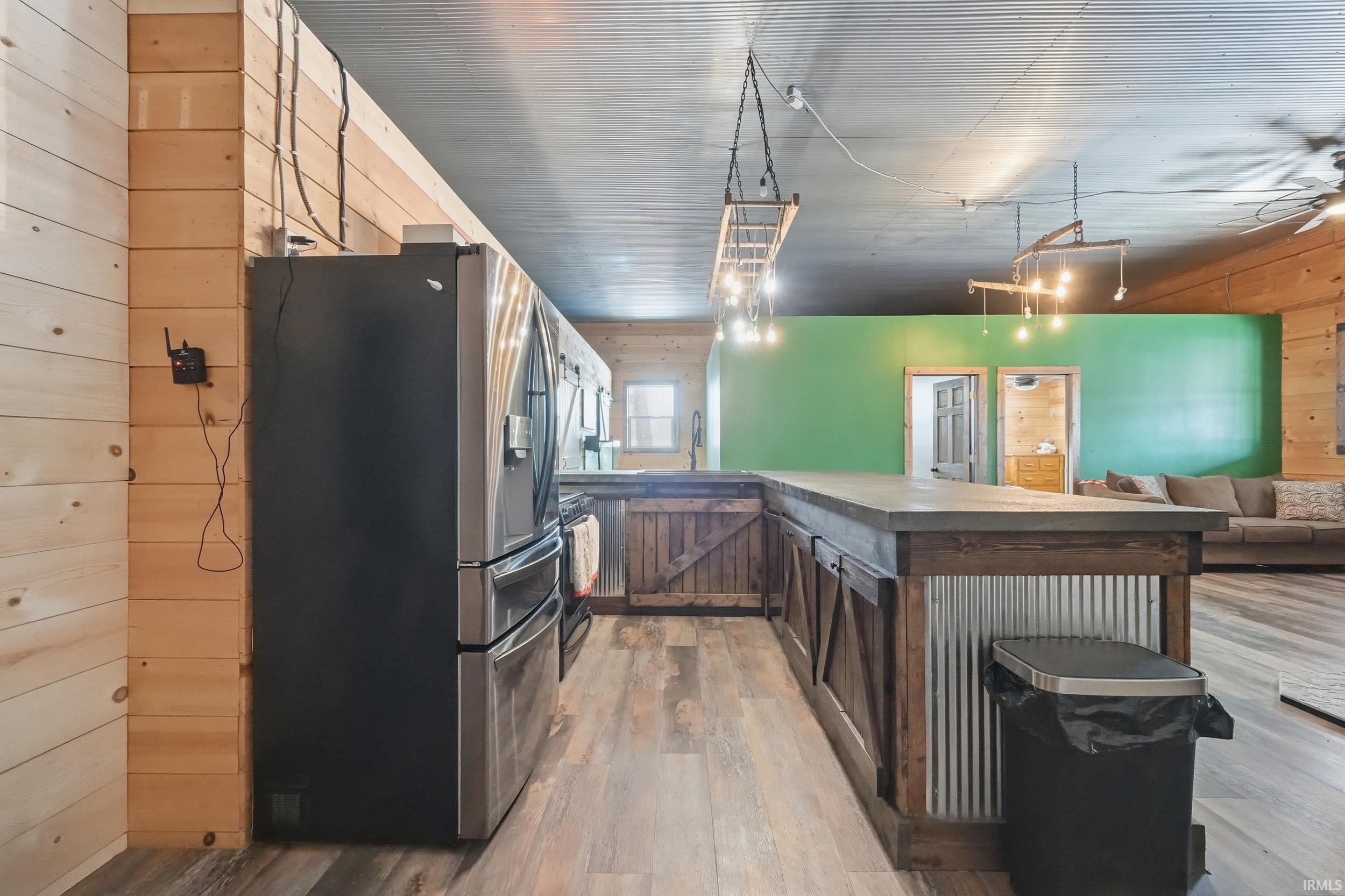 Kitchen featuring wood walls, stainless steel fridge, light wood-type flooring, open floor plan, and dark brown cabinets