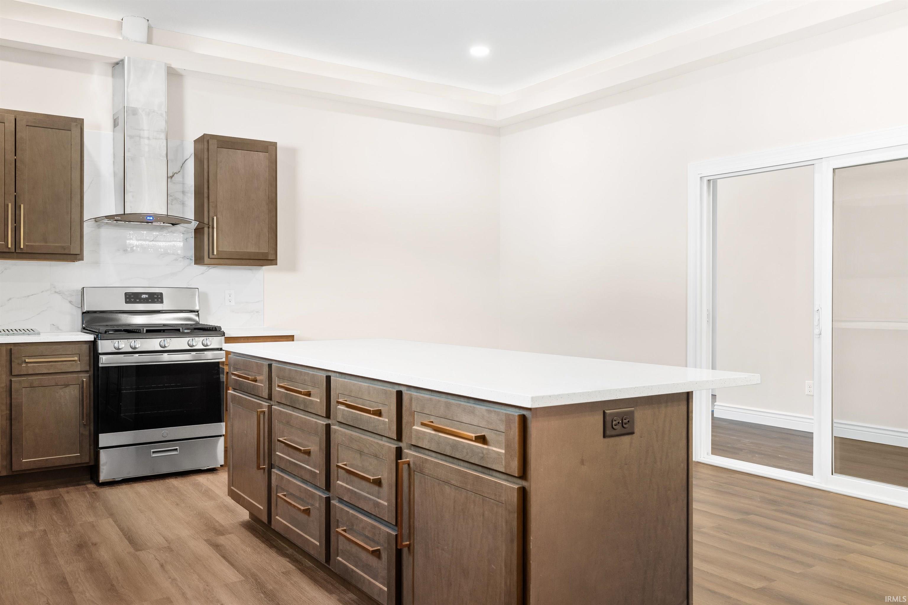 Kitchen featuring stainless steel gas range oven, wall chimney range hood, light wood-style floors, a center island, and recessed lighting
