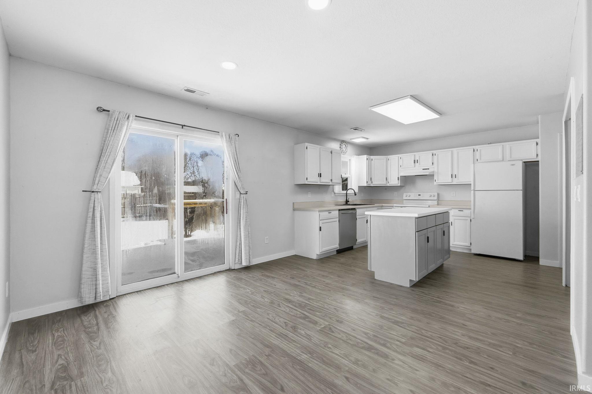 Kitchen featuring white appliances, light countertops, a kitchen island, white cabinetry, and dark wood-style floors