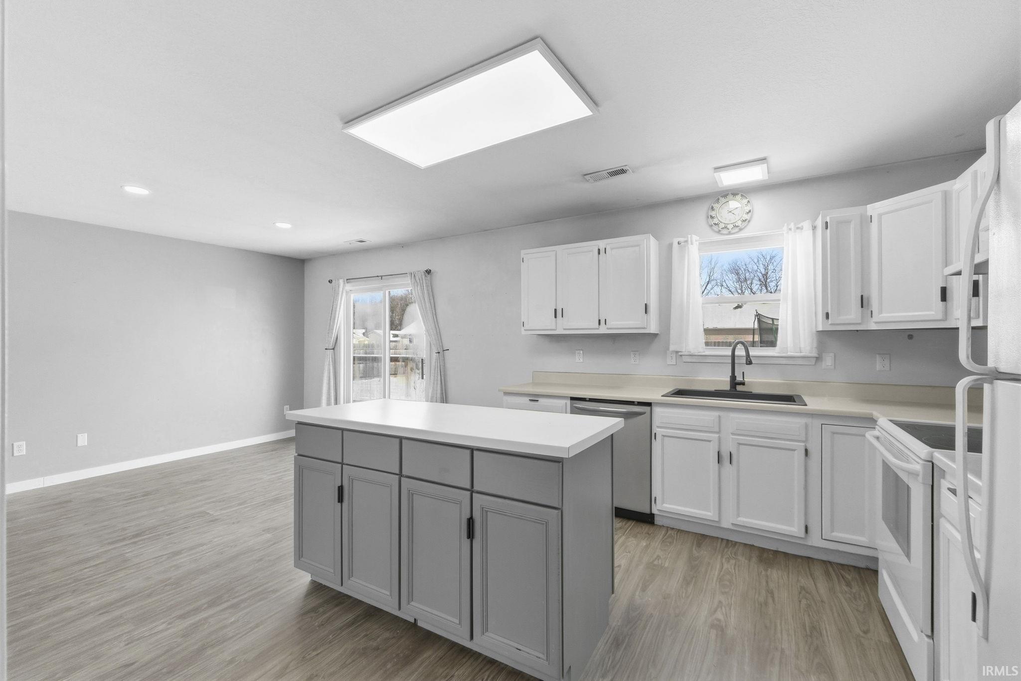 Kitchen featuring white cabinetry, white appliances, light countertops, a kitchen island, and recessed lighting