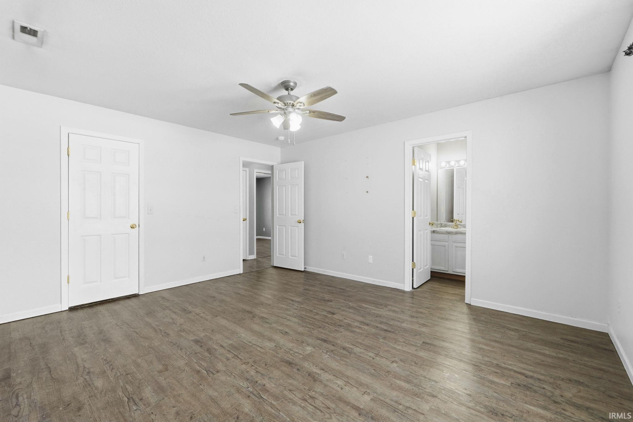 Unfurnished bedroom with ceiling fan, dark wood finished floors, and ensuite bath