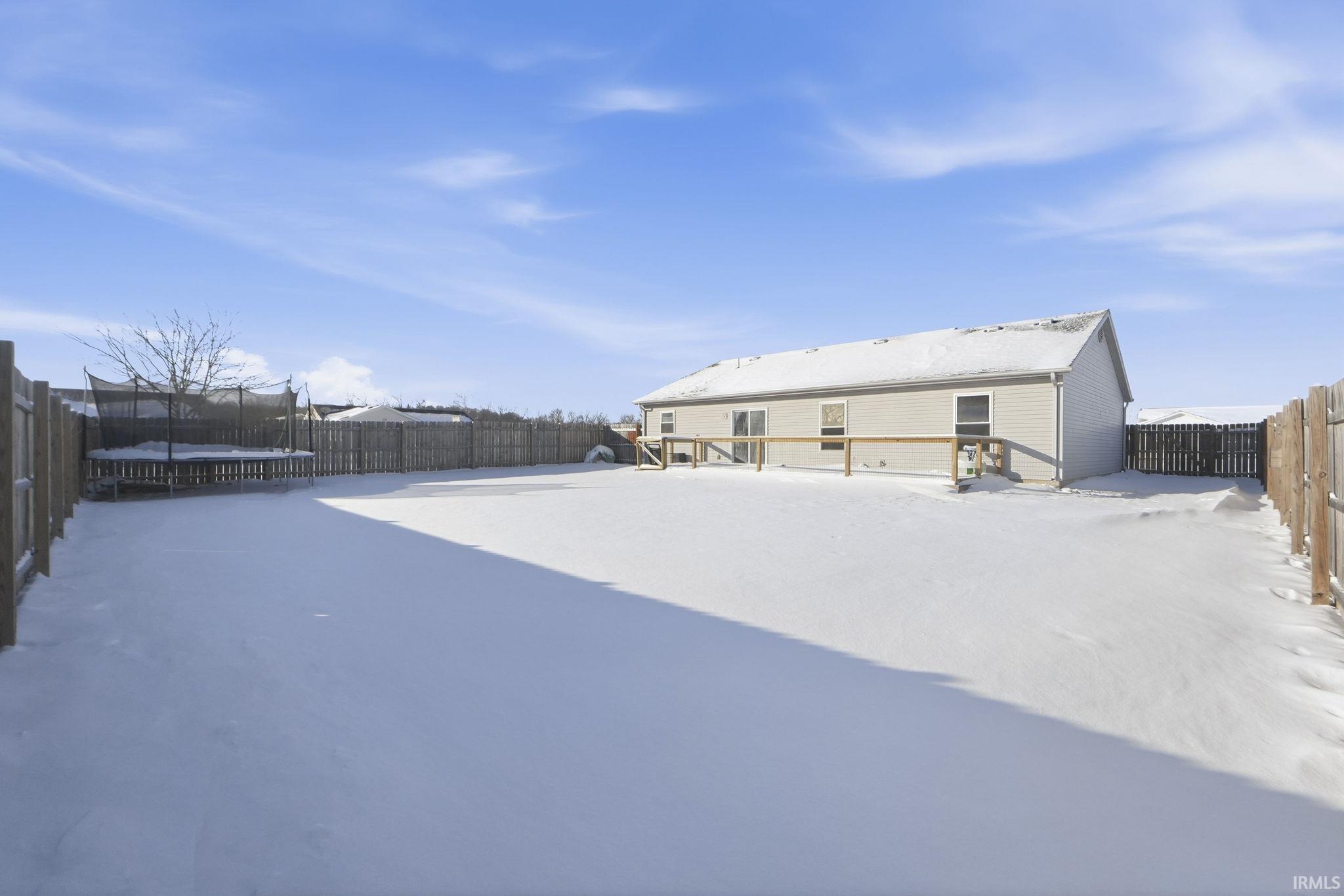 Snow covered back of property featuring a fenced backyard and a trampoline