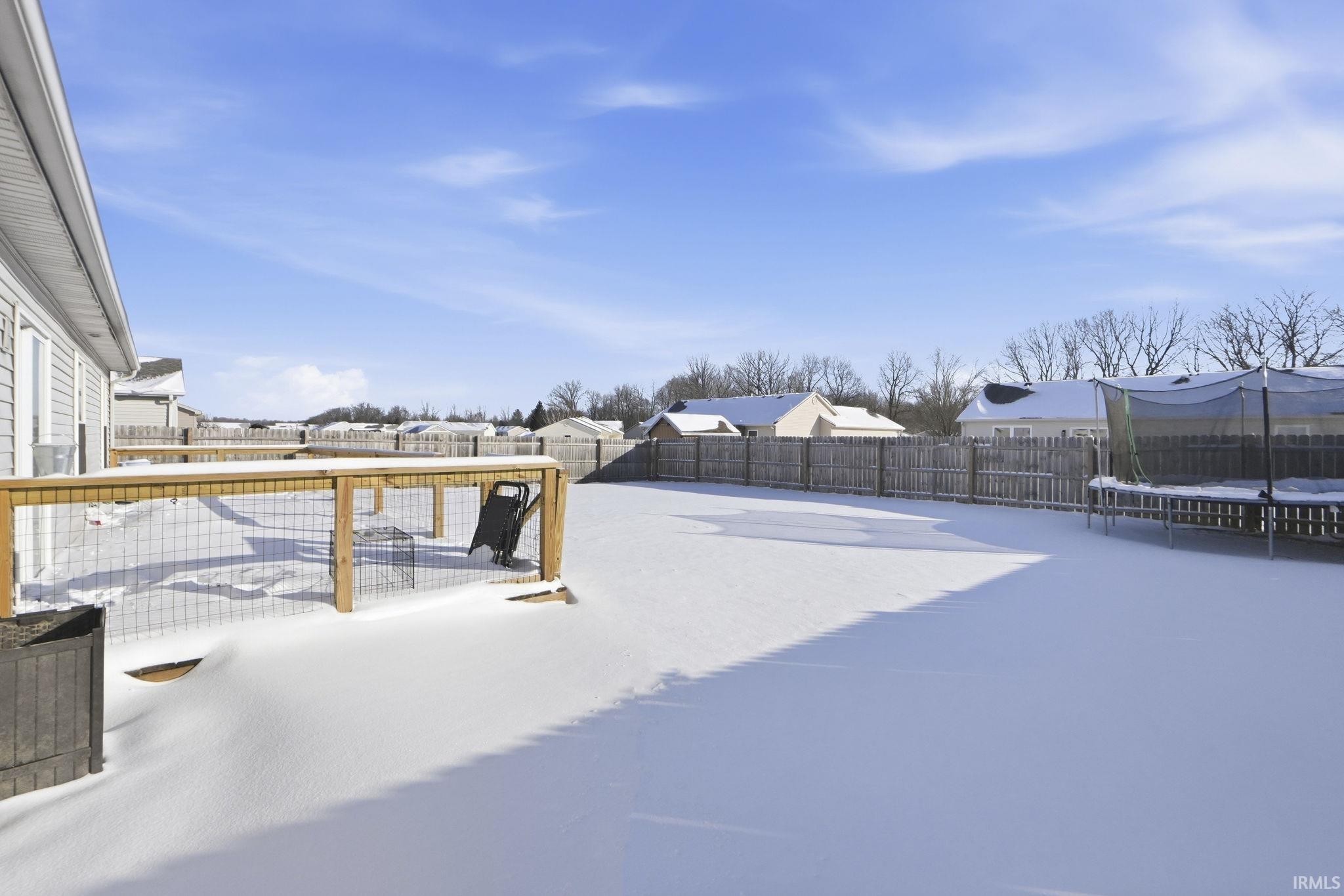 Yard covered in snow with a residential view, a fenced backyard, a trampoline, and a deck