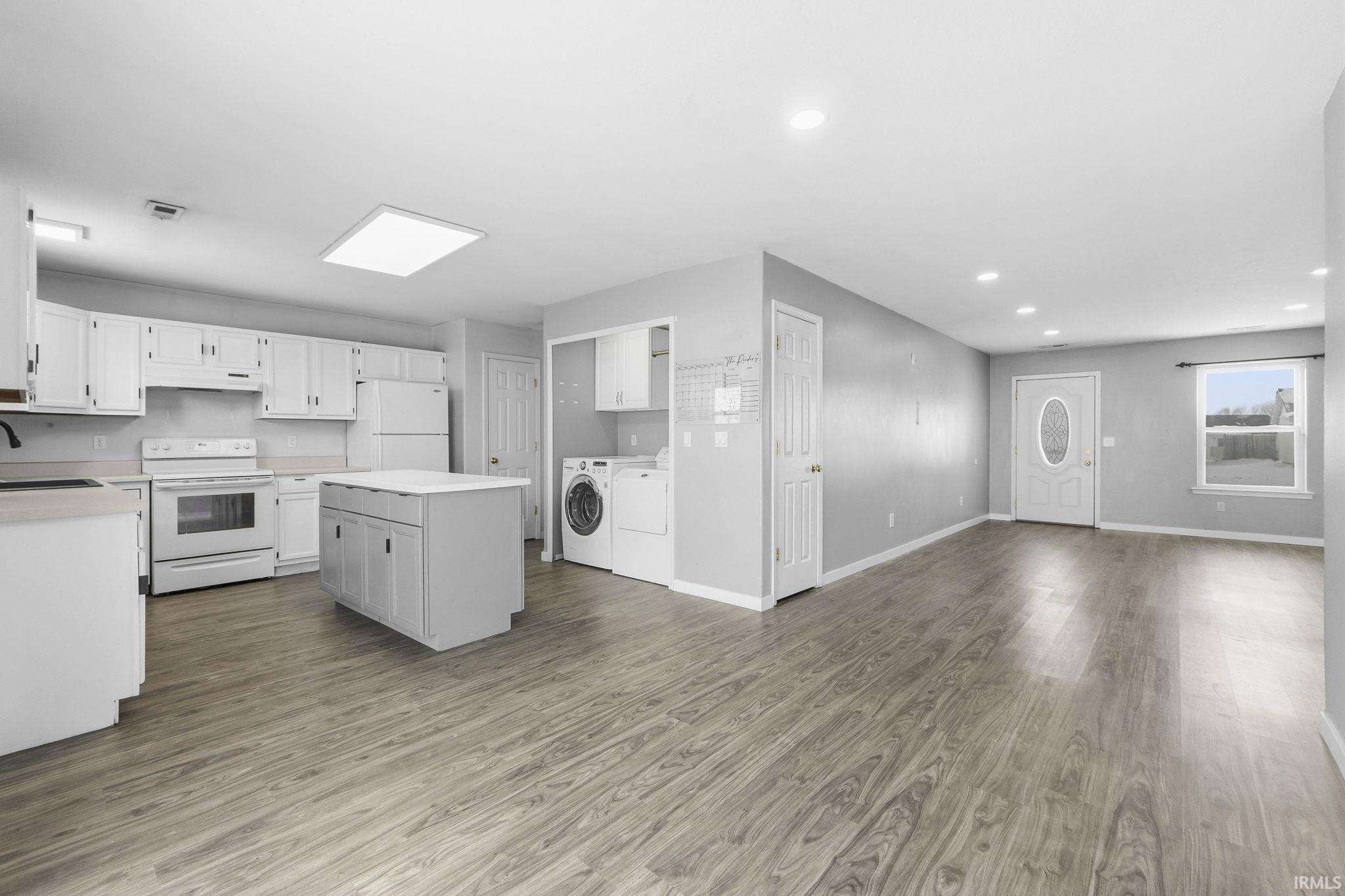 Kitchen featuring white appliances, washing machine and clothes dryer, light countertops, white cabinetry, and open floor plan