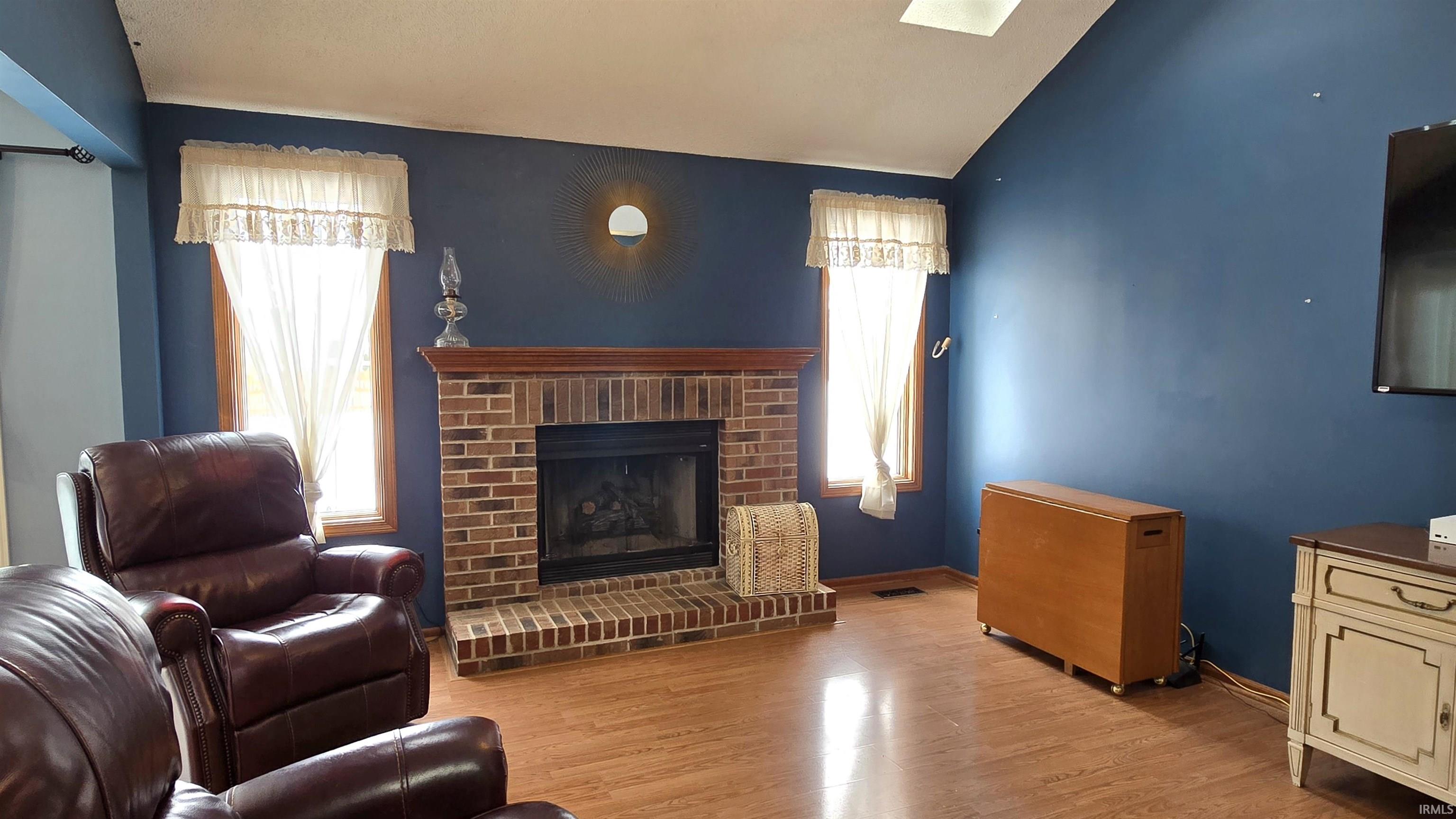 Living room with light wood-style flooring, a fireplace, a skylight, and lofted ceiling