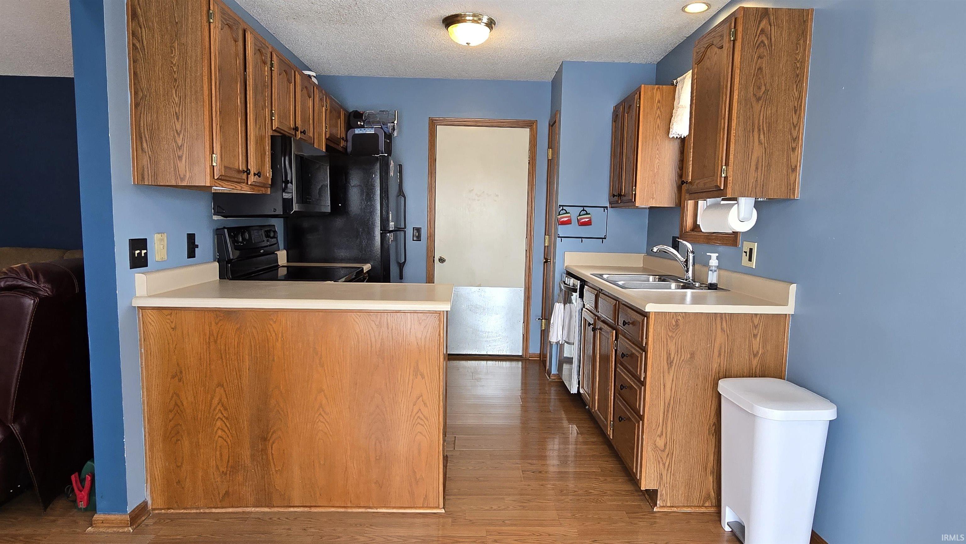 Kitchen with brown cabinetry, light countertops, light wood-style flooring, and a textured ceiling