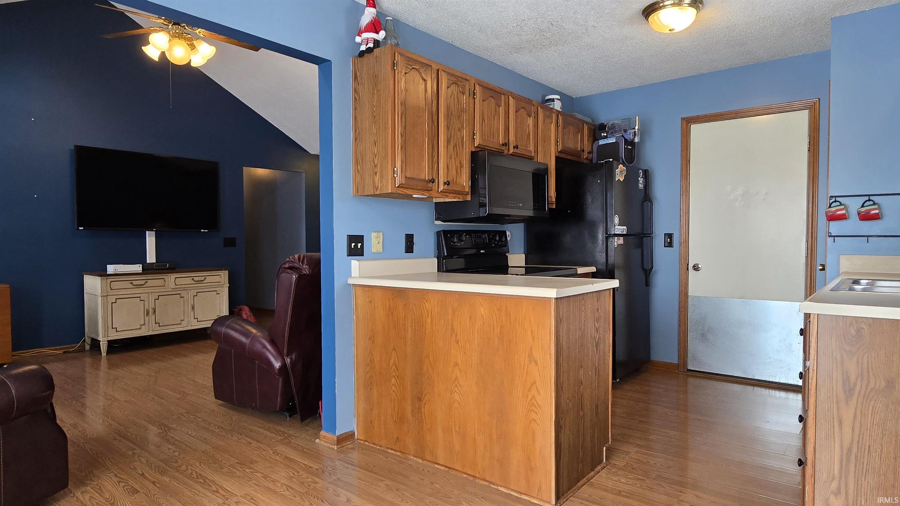 Kitchen with open floor plan, brown cabinetry, light countertops, light wood finished floors, and a textured ceiling