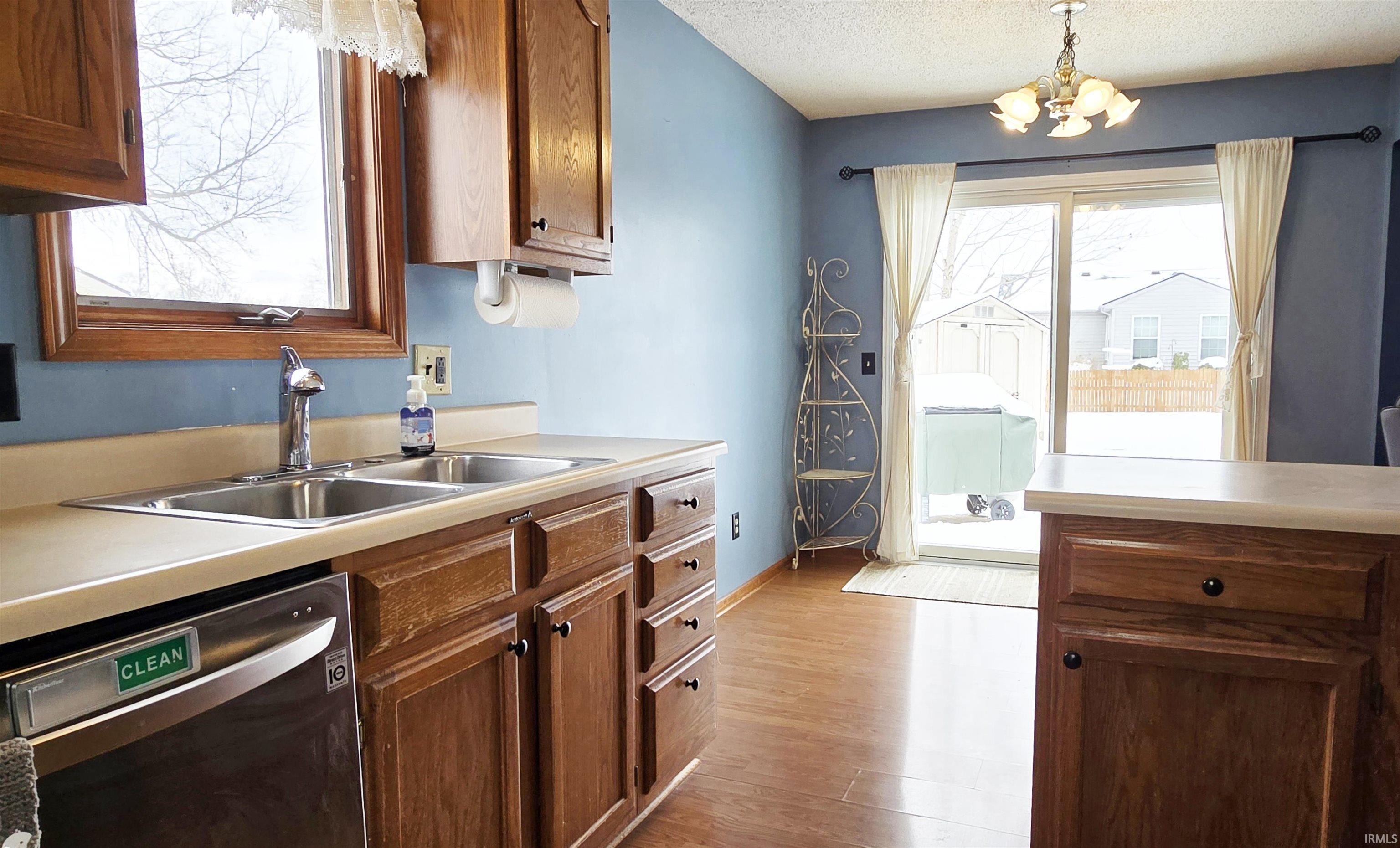 Kitchen featuring a chandelier, stainless steel dishwasher, a textured ceiling, hanging light fixtures, and light countertops